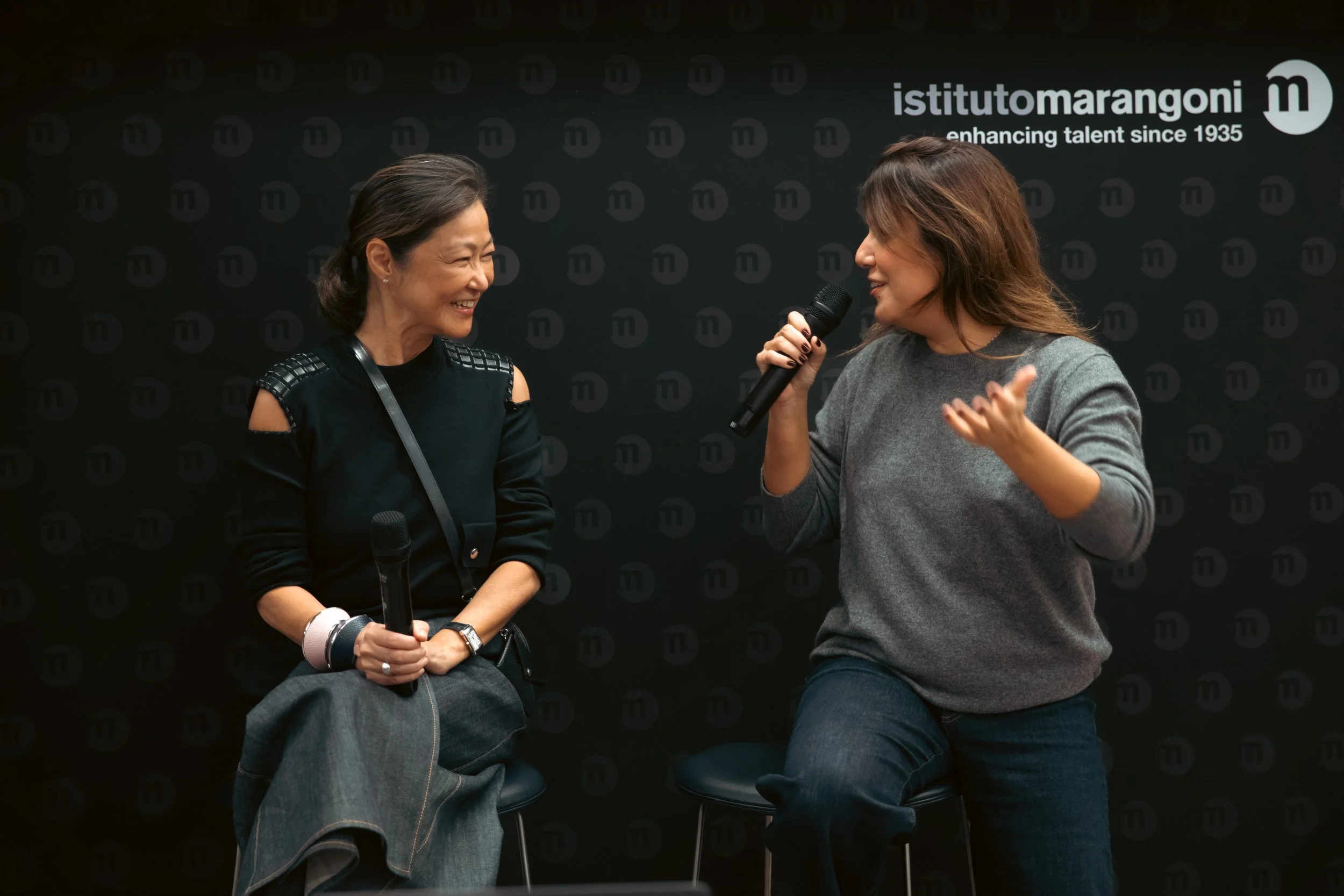Deux femmes discutent en séance avec microphones, en arrière-plan un panneau noir avec le logo de l'Institut Marangoni et le texte "enhancing talent since 1935".