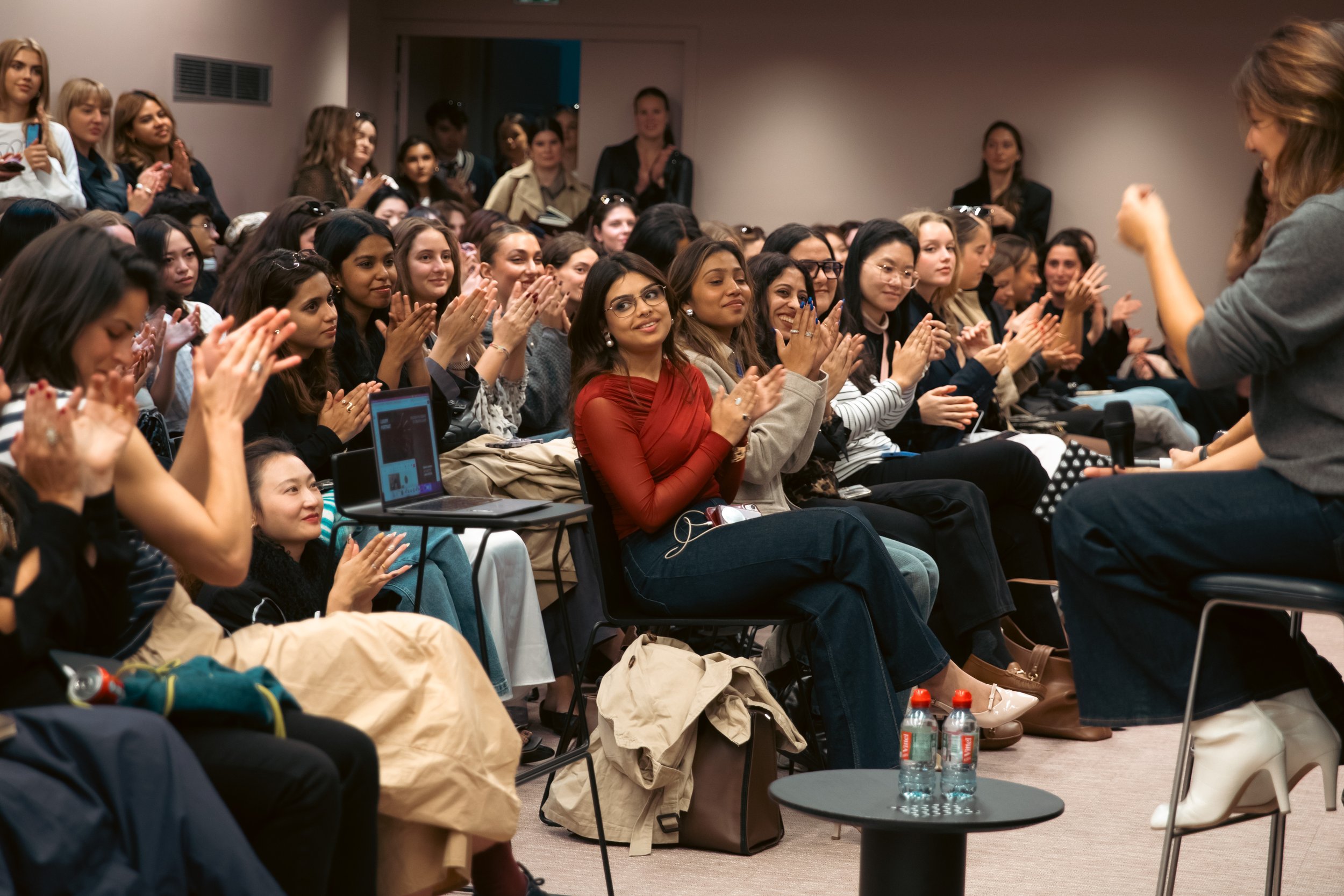 Une femme face à un groupe d'adolescentes lors d'une conférence ou atelier, applaudissant et souriant.