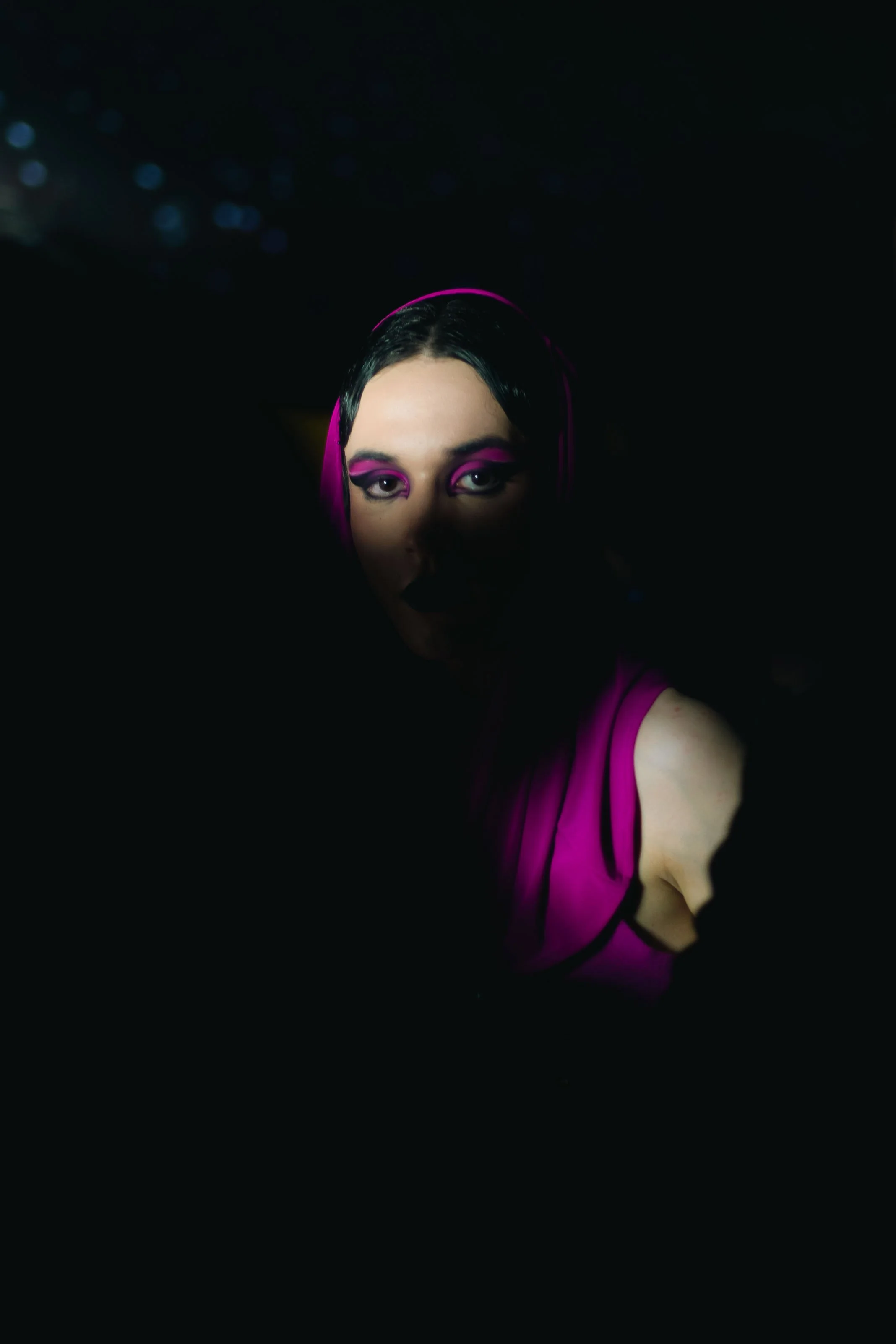 Portrait d'une femme avec maquillage violet et écharpe rose dans l'obscurité, éclairée partiellement