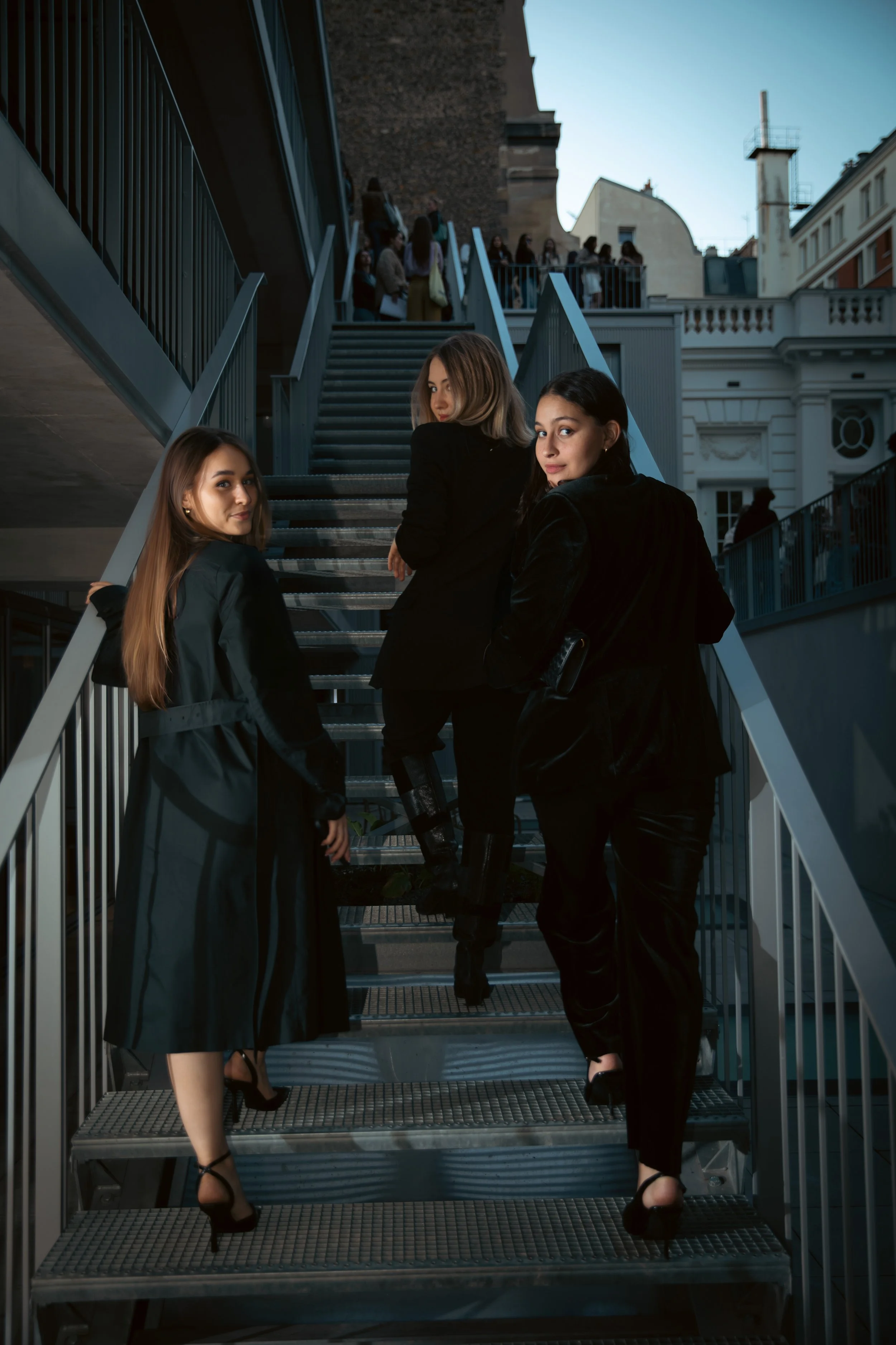 Trois femmes habillées élégamment montent des escaliers extérieurs la soirée.