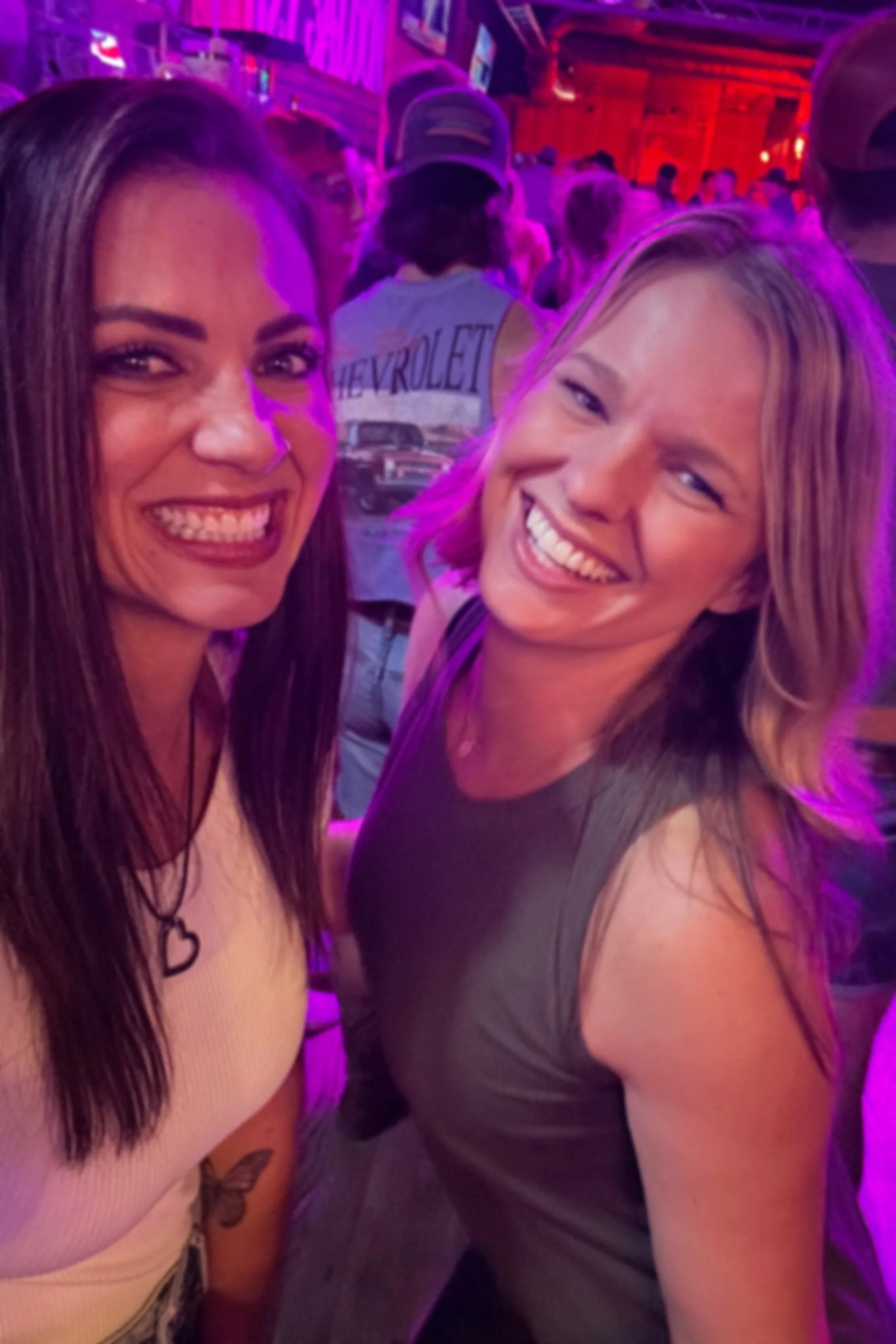 Two women smiling and having fun in a colorful indoor setting with purple backlight.
