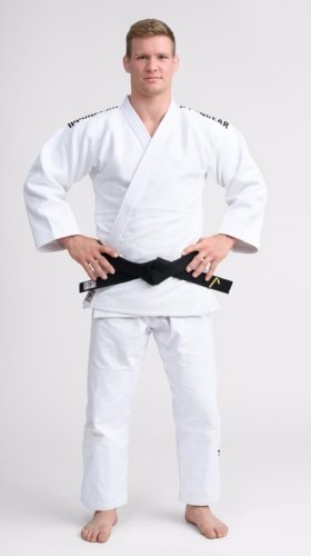 Man wearing a white judo gi with a black belt, standing with hands on hips against a plain white background.