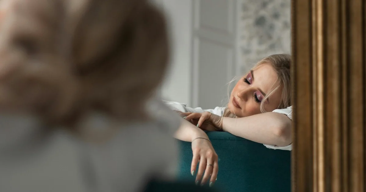 Mujer apoyada en un sofá mirando pensativa su reflejo en un espejo, representando la búsqueda de sentido emocional