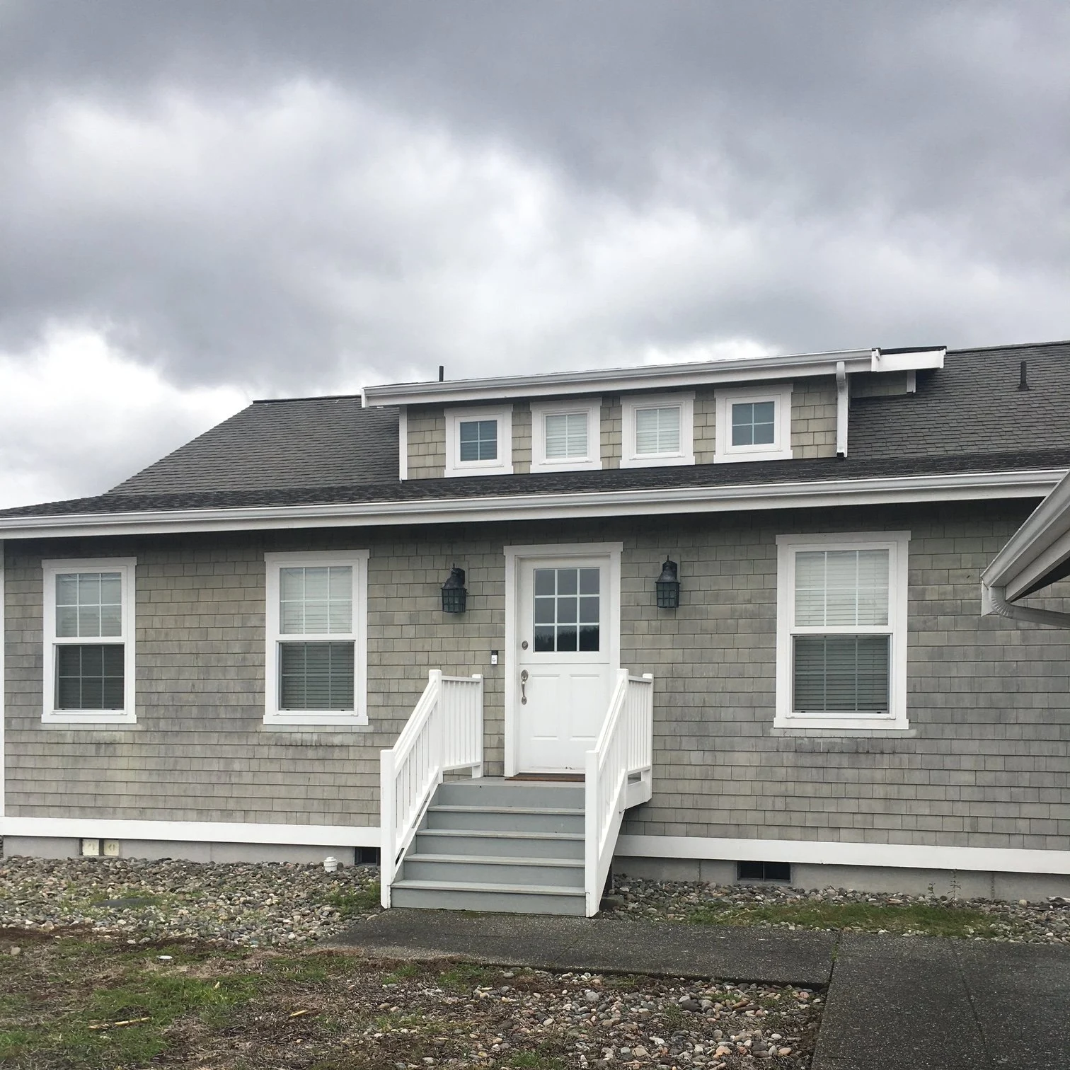 Grey wood-sided house with seven windows in front of a stormy grey sky