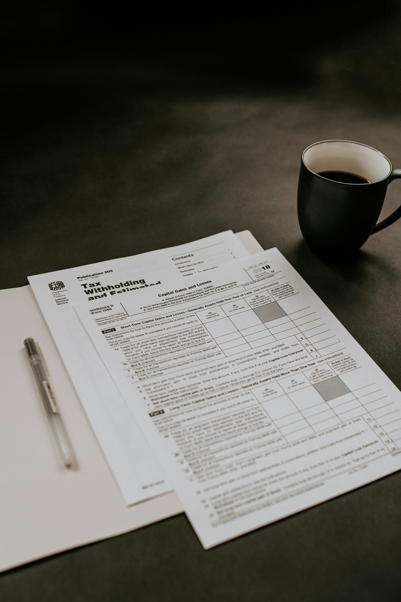 A desk with a tax form, a pen on a white notepad, and a cup of coffee on a black surface.