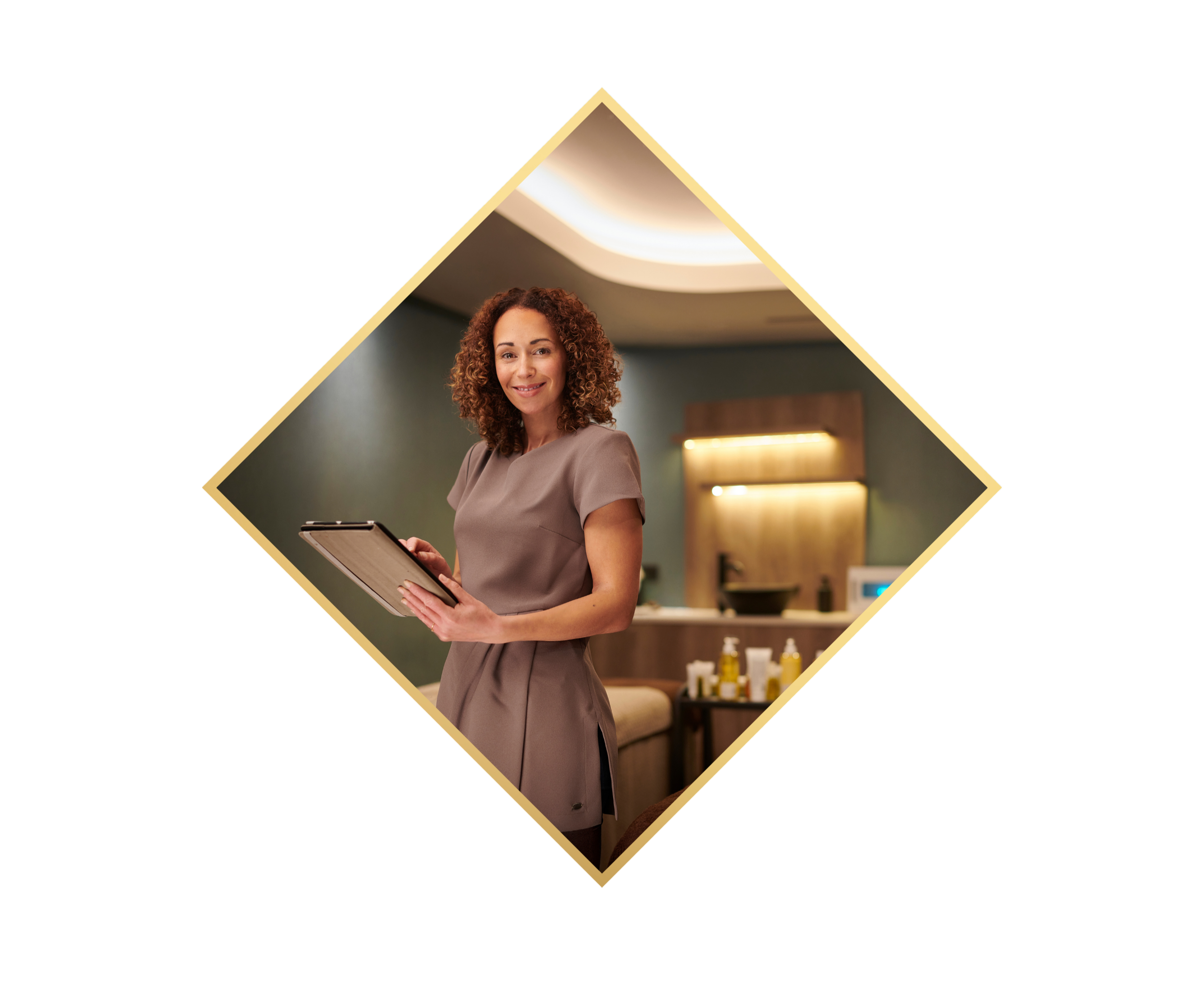 A woman with curly hair smiling while holding a clipboard, standing indoors with a reception or lounge area in the background.