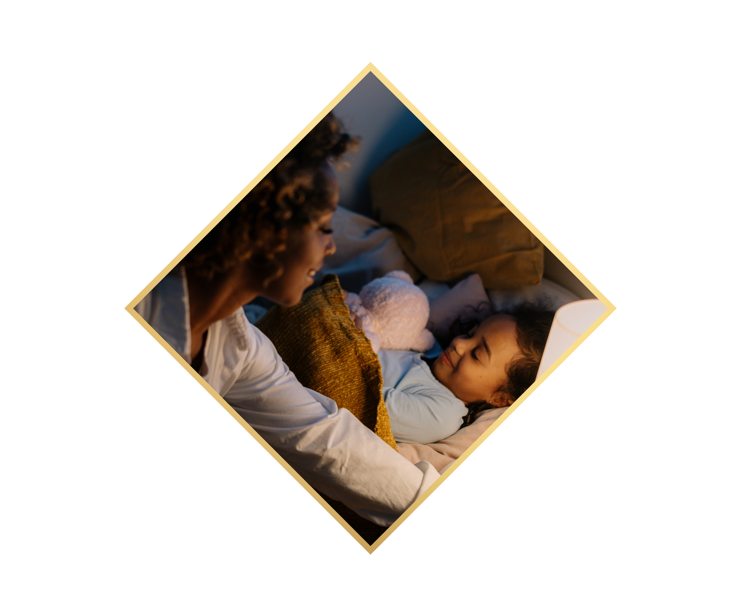 A woman and a young girl are lying in bed, smiling at each other in a cozy, warmly lit bedroom.