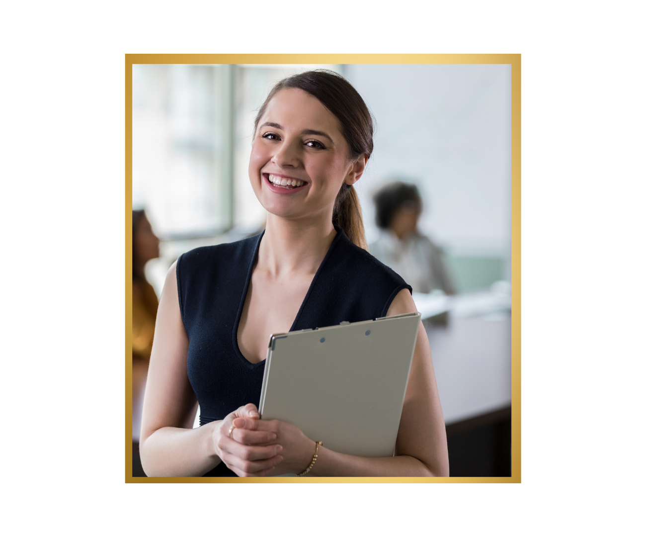 A young woman in a professional setting holding a clipboard, smiling at the camera with other people blurred in the background.