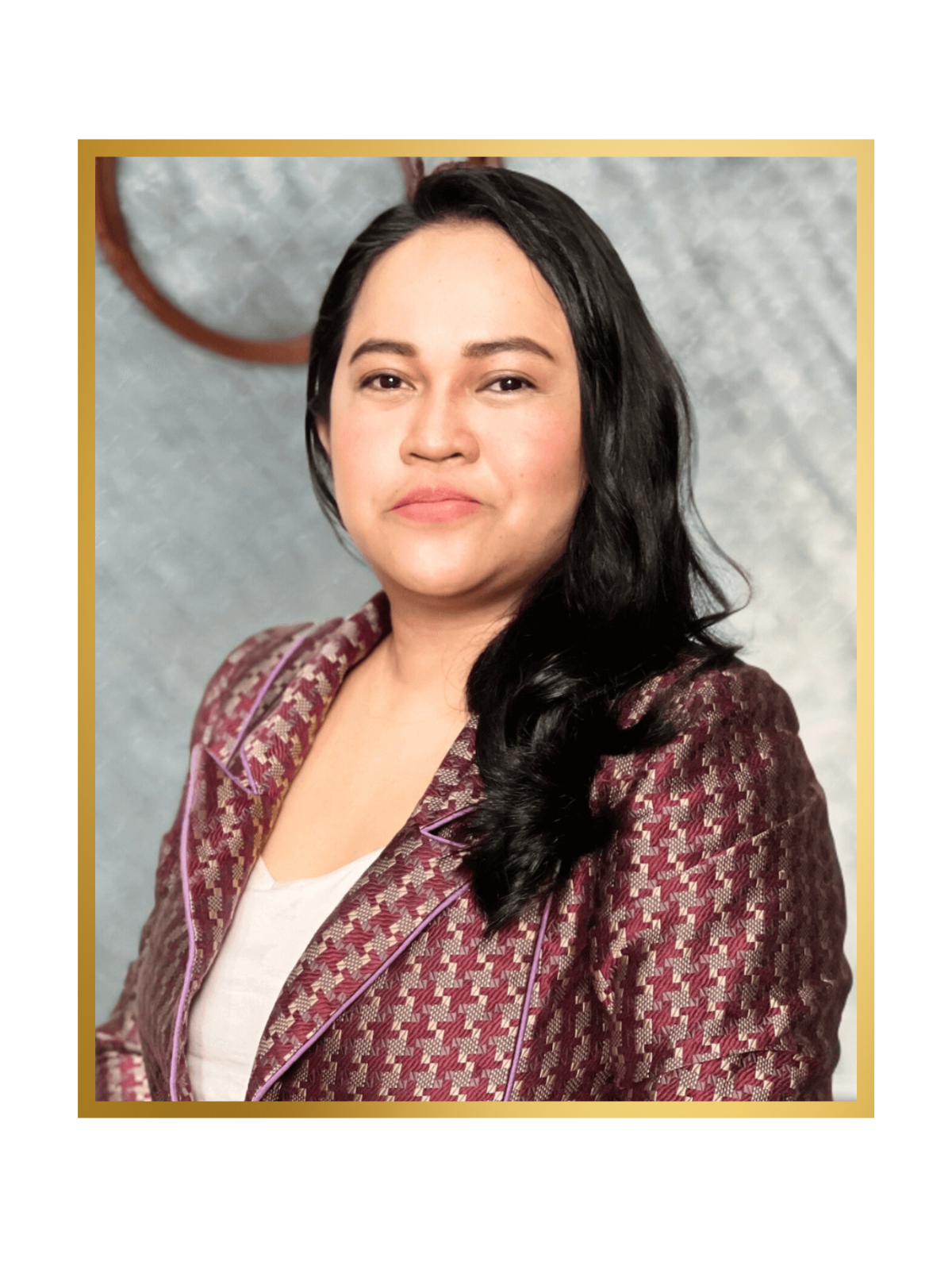 Professional portrait of a woman with long black hair, wearing a patterned maroon blazer and white top, against a grayish textured background.