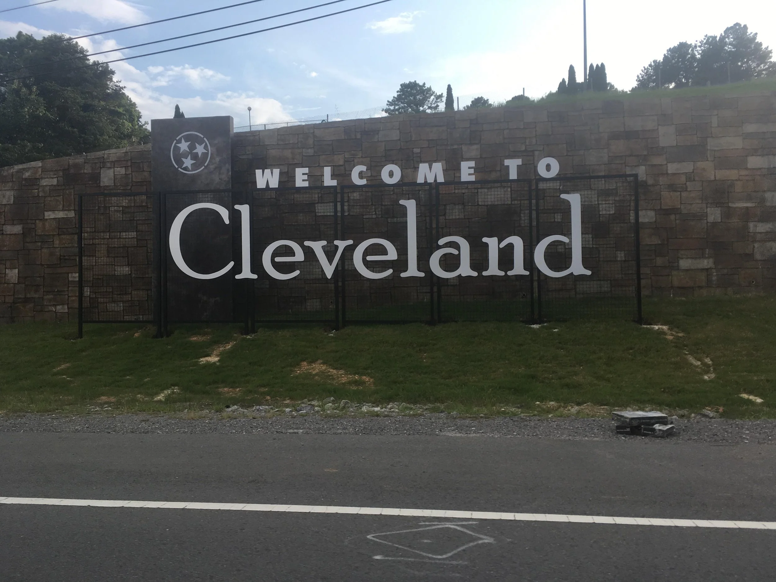 Welcome to Cleveland sign on a stone wall, with a cloudy sky and some trees in the background.