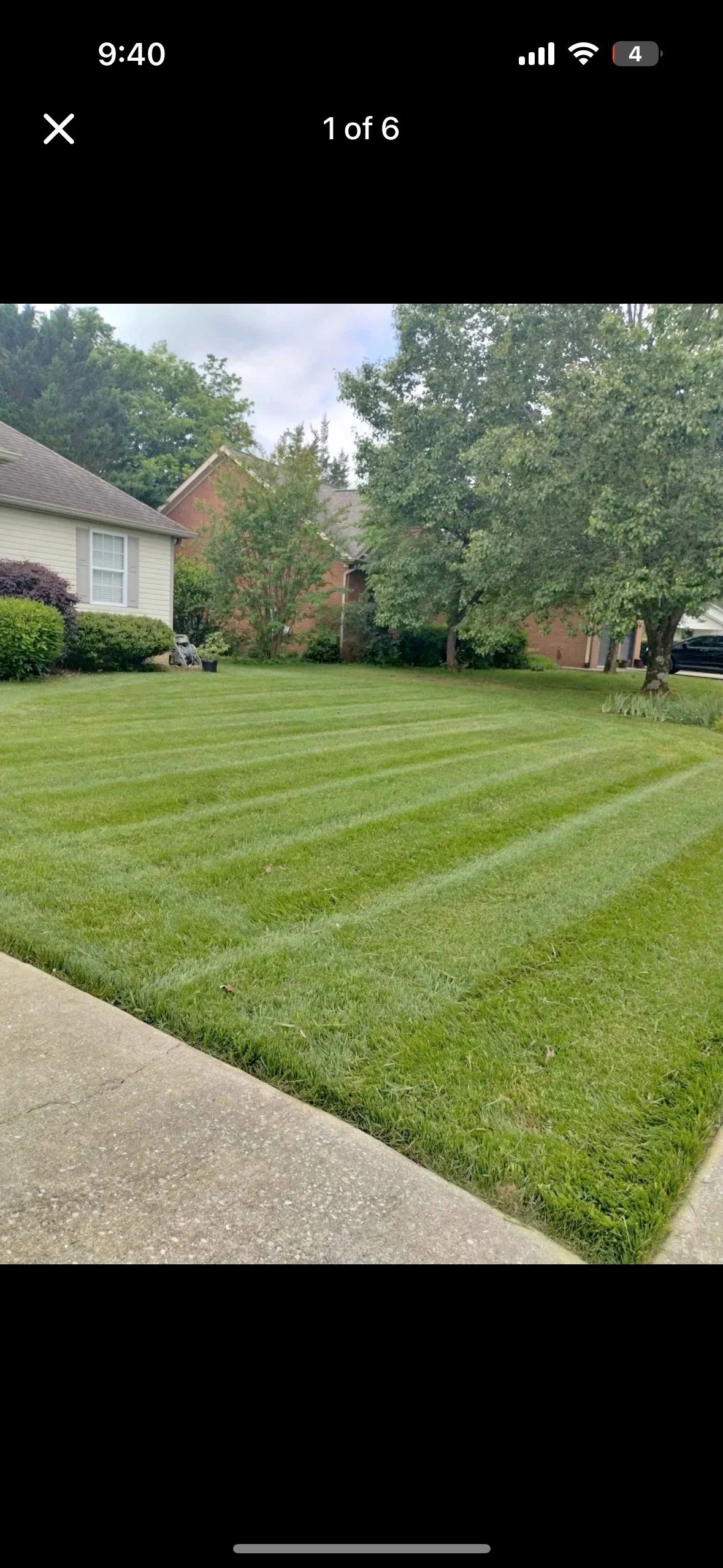 A well-maintained lawn with freshly mowed grass and visible striped patterns, adjacent to a concrete sidewalk, with houses and trees in the background.
