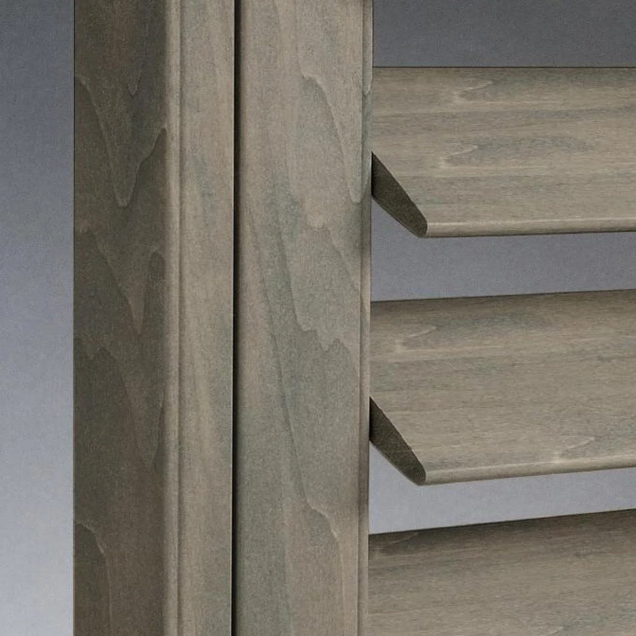 Close-up of a wooden cabinet door with light-colored wood grain and a black handle, set against a gray wall.