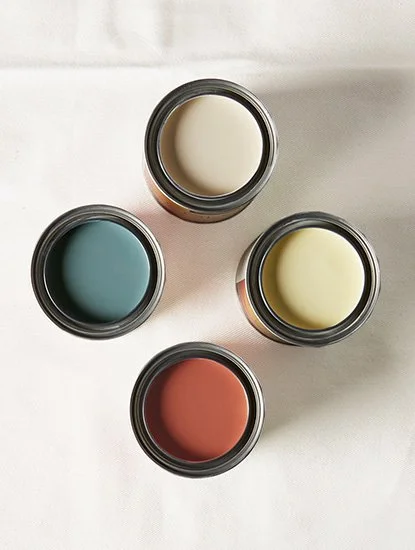 Four open small jars containing different colored creams or pastes, arranged on a white surface.