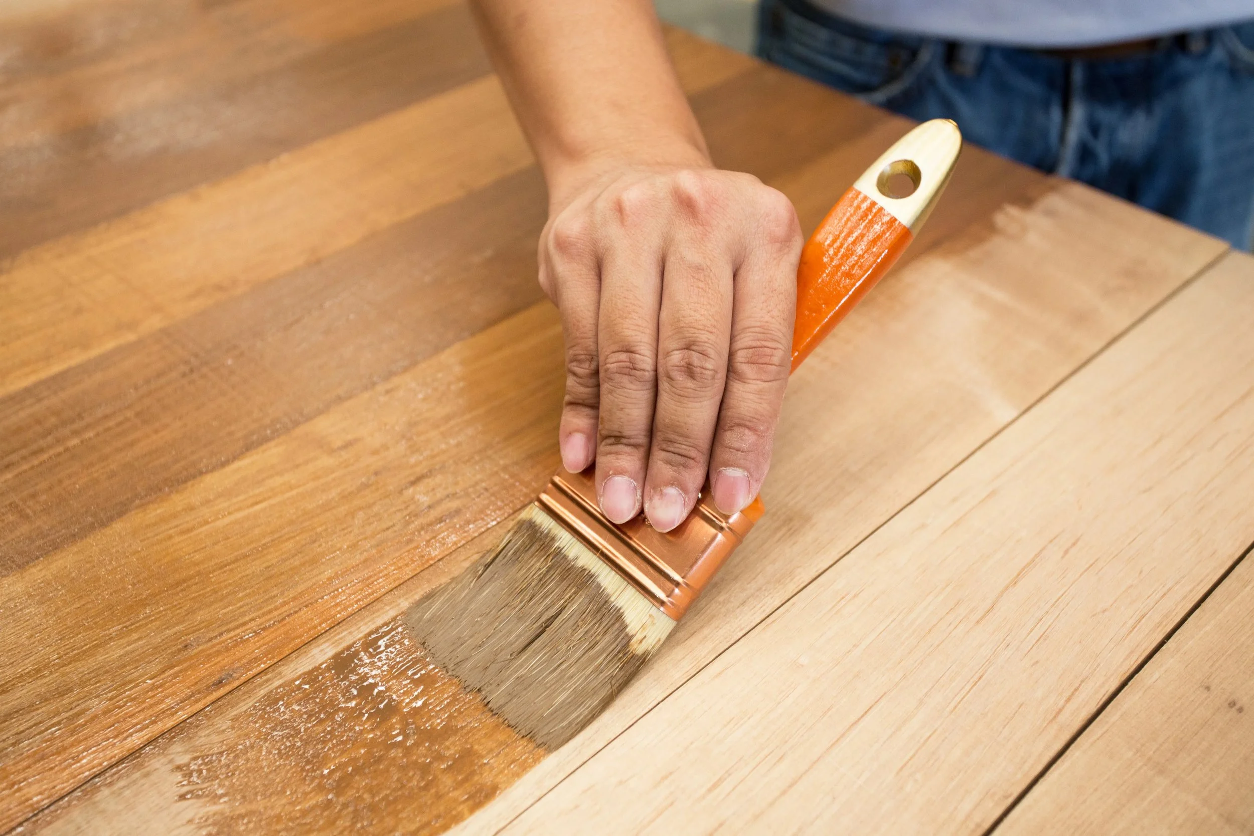 Person applying stain to a wooden table with a paintbrush.