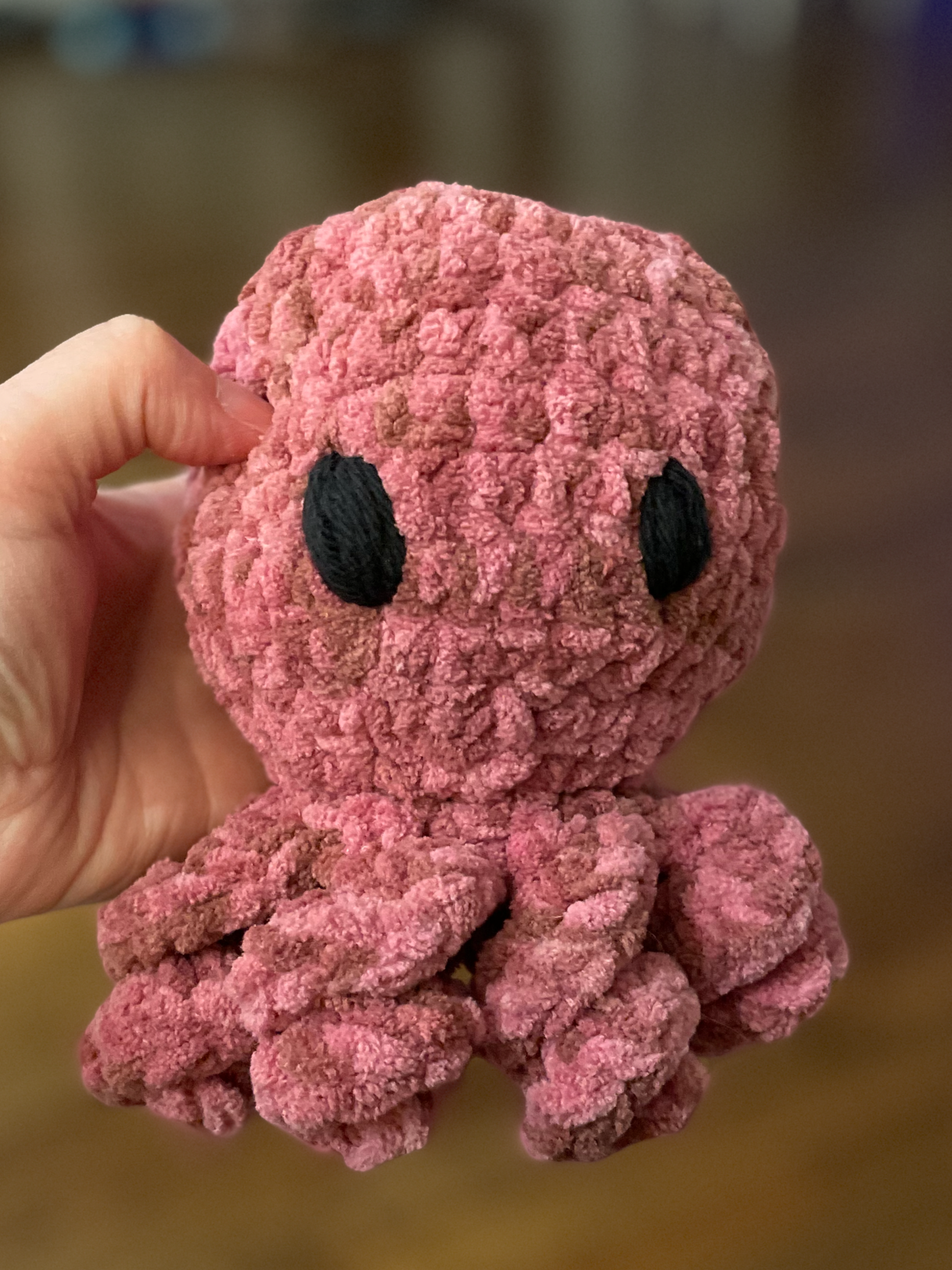 pink crochet octopus with black eyes held by a hand