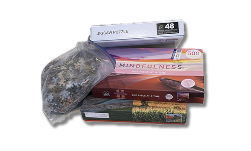 pile of puzzles in boxes and one bag of puzzle pieces next to it