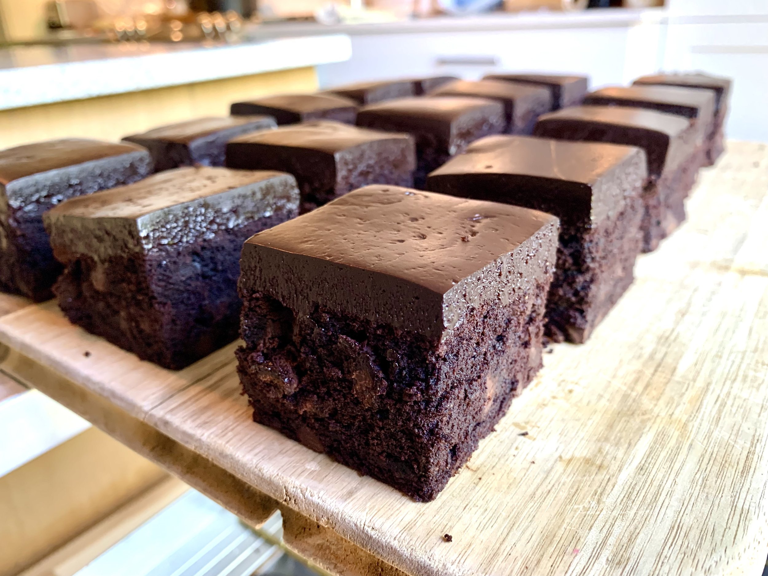 Close-up of multiple chocolate brownies with a shiny chocolate glaze on top, arranged on a wooden surface.