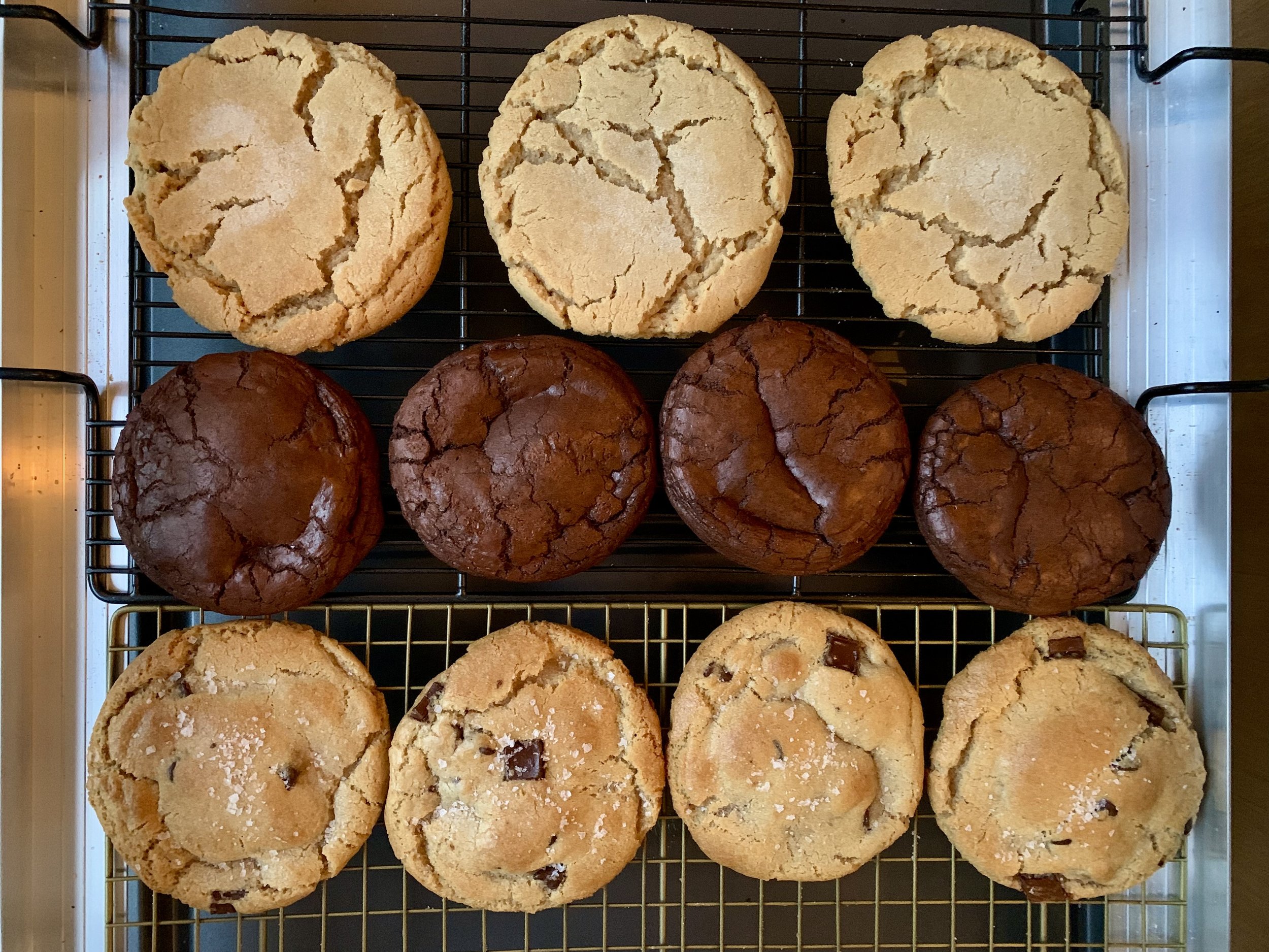 A baking tray with three types of cookies: sugar cookies with salt on top at the bottom, chocolate chip cookies in the middle, and crackle cookies at the top, arranged in three rows.