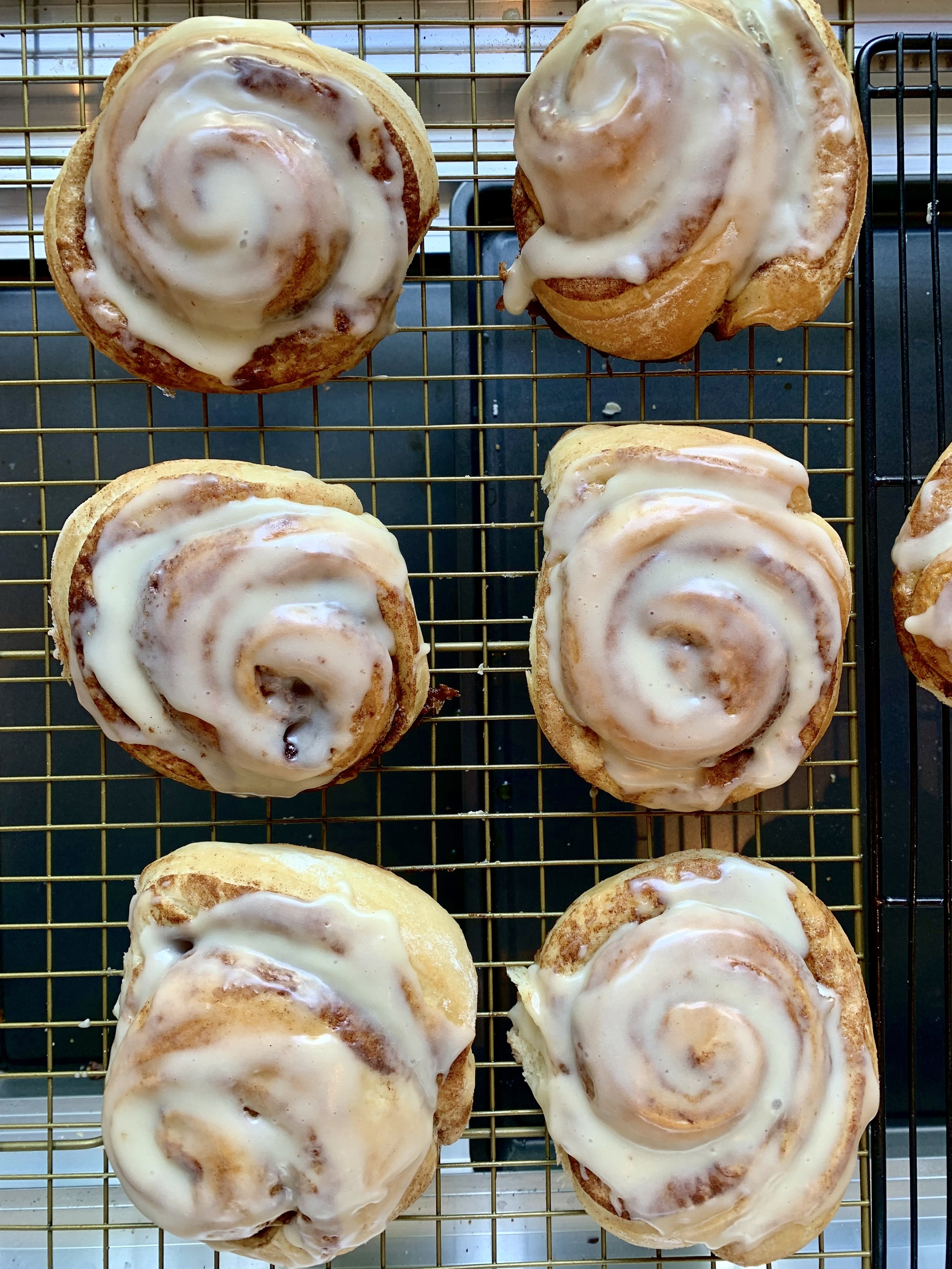 Six cinnamon rolls with icing on a cooling rack.