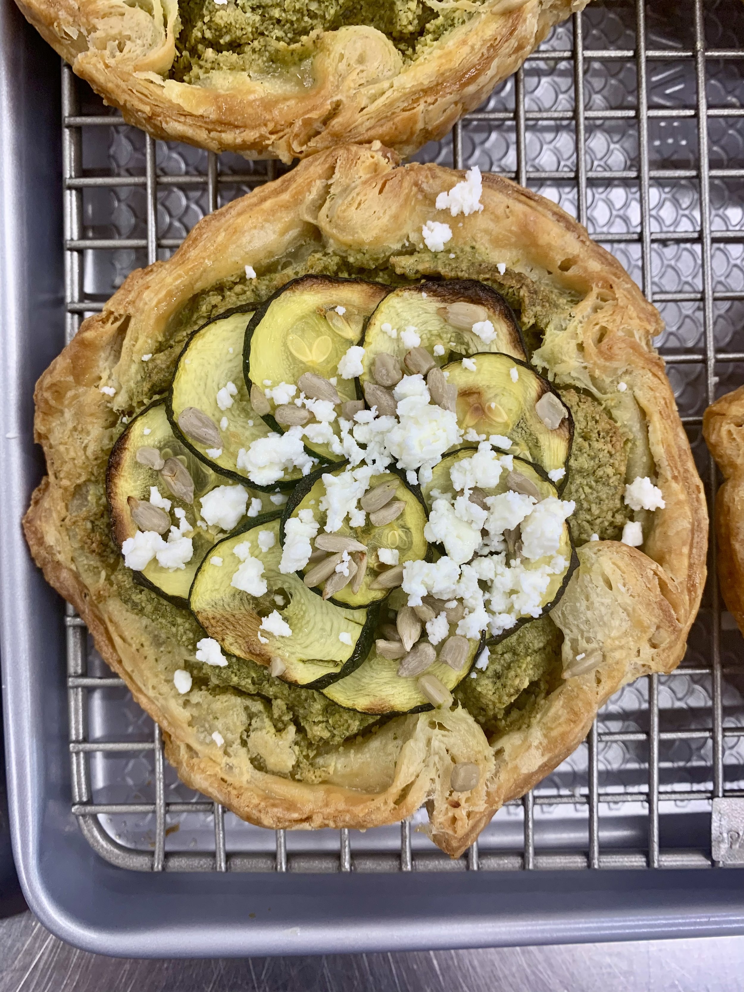 A savory galette pastry topped with sliced zucchini, crumbled feta cheese, and sunflower seeds, placed on a cooling rack.