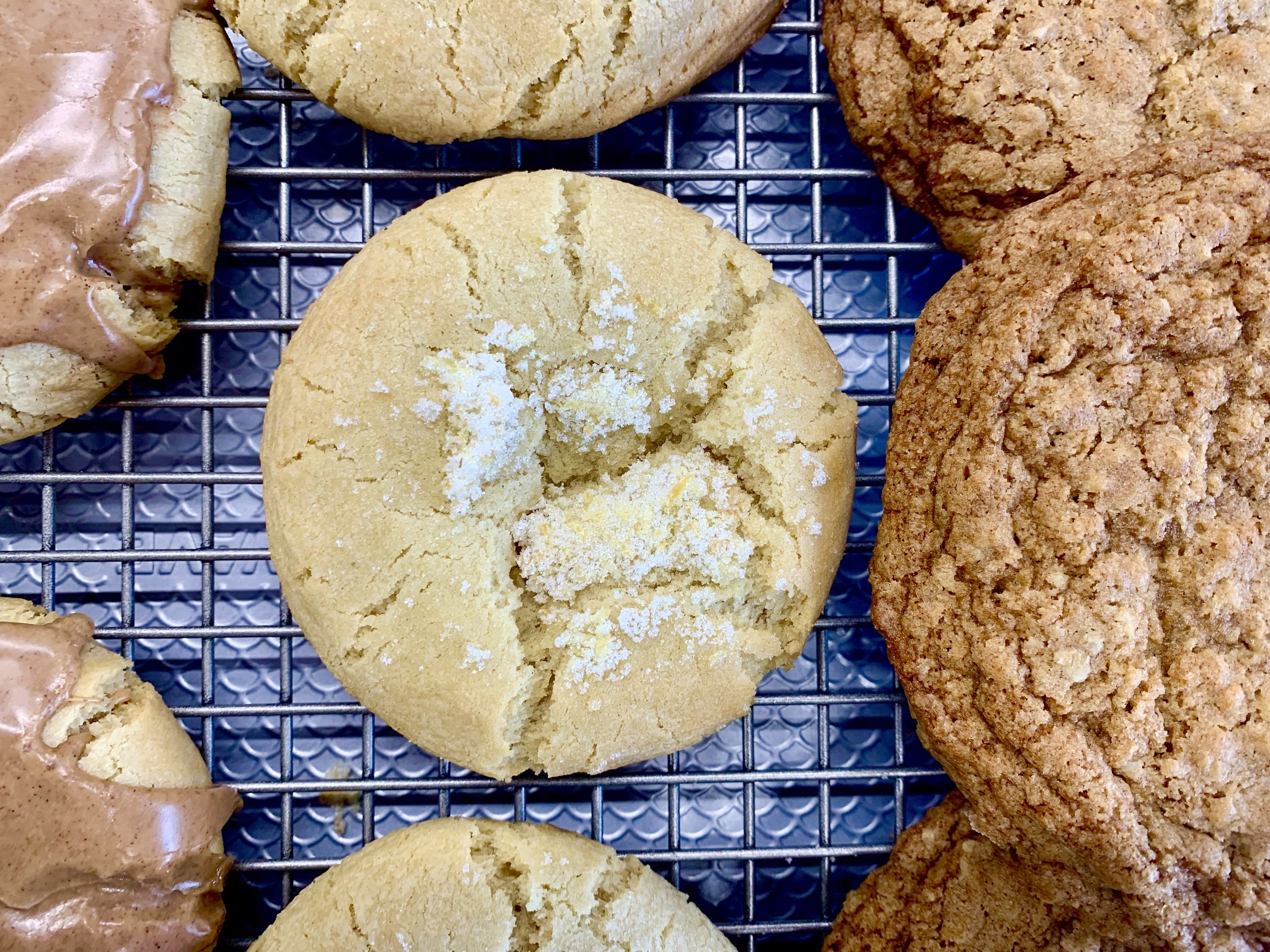 Close-up of freshly baked cookies on a cooling rack, including sugar cookies, chocolate chip cookies, and oatmeal cookies.