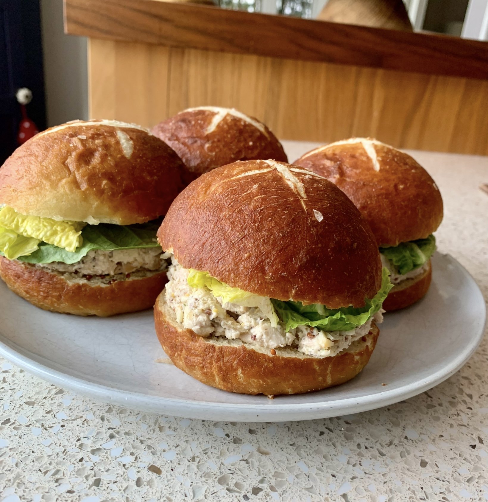 Four dijon chicken salad sandwiches on pretzel buns with lettuce