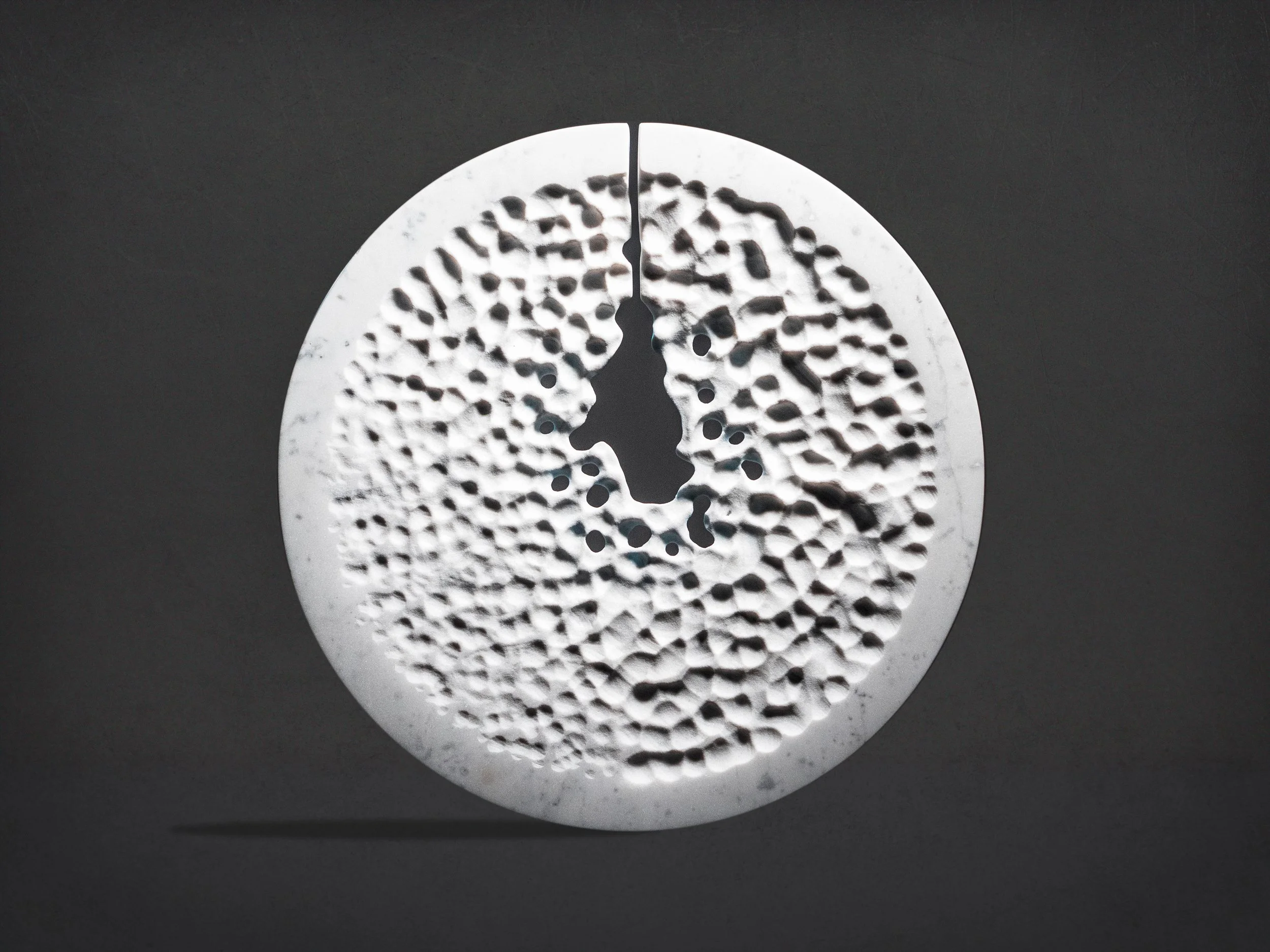 Objet rond en blanc avec un motif perforé complex et texturé, posé sur un fond gris foncé.