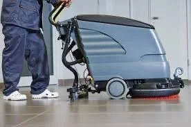 Person standing next to a large commercial floor cleaning machine.