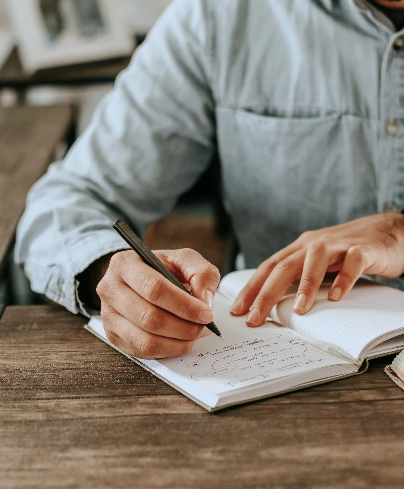 Person writing in a notebook with a pen at a wooden table