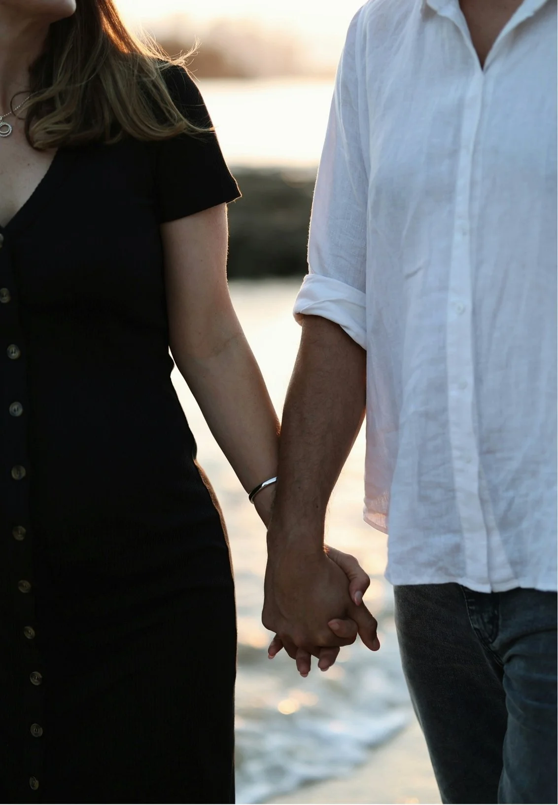 A couple holding hands at a beach during sunset.