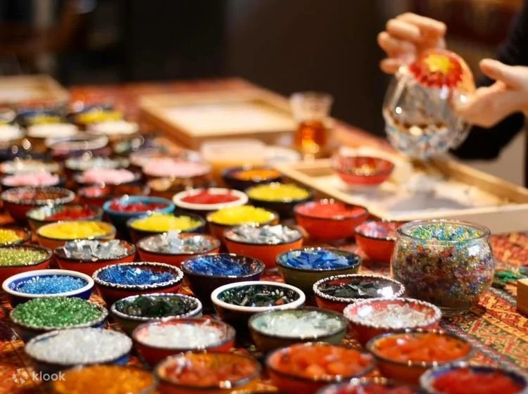 A table filled with small bowls of colorful glass beads and jewelry-making supplies.