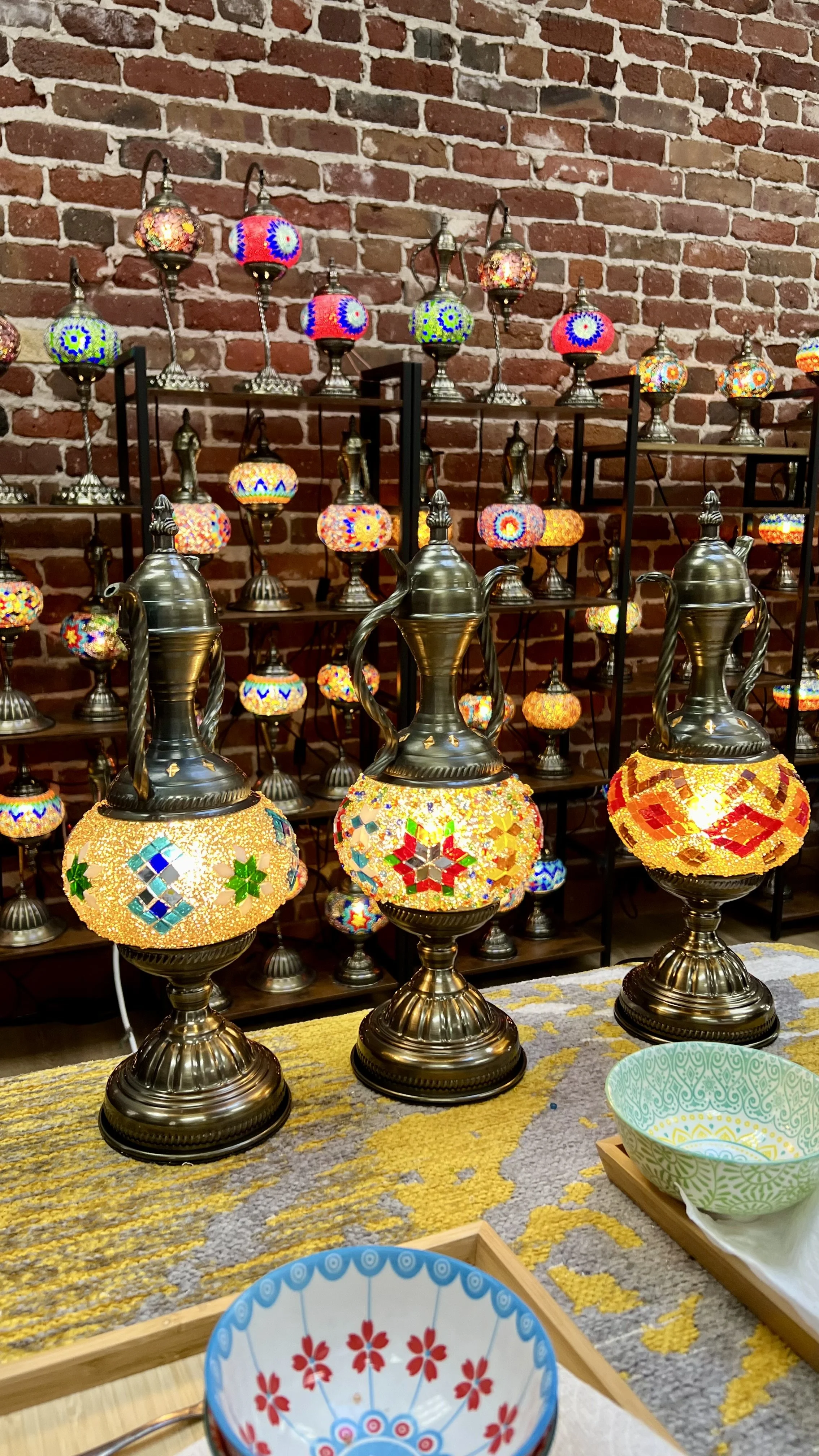 Colorful Turkish mosaic lamps displayed on a table against a brick wall.