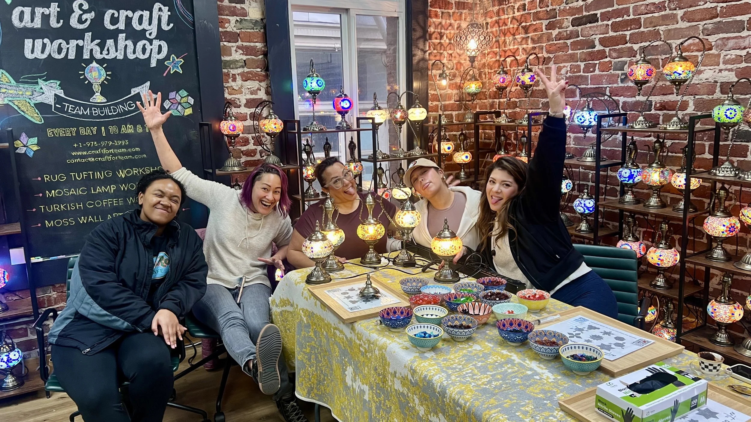 Group of five women at an art and craft workshop, displaying colorful lamps and decorative bowls.