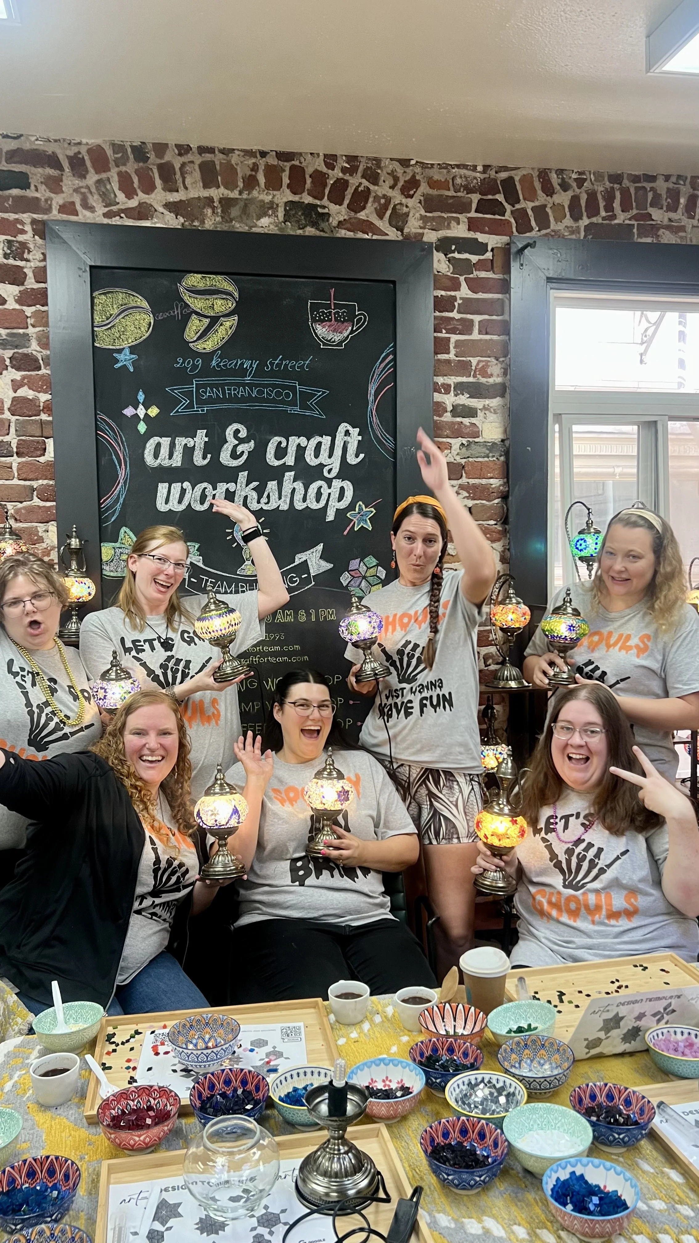 Group of women at a craft workshop, holding colorful mosaic lamps inside a cafe with a chalkboard sign behind them reading 'art & craft workshop' at 209 Kearny Street, San Francisco.