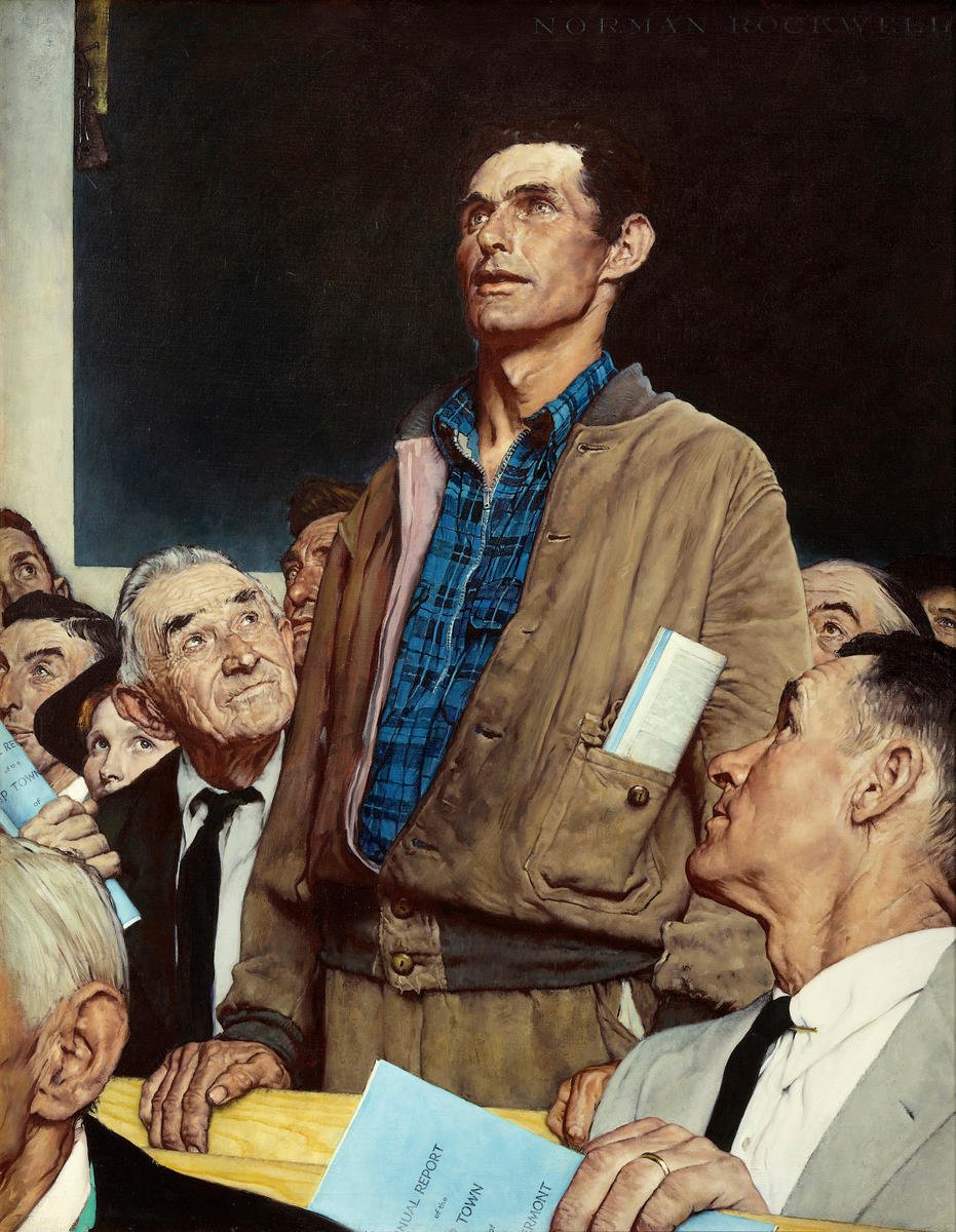 A portrait of a man in a tan jacket and blue plaid shirt standing among seated and standing people, holding a book or report, with a group of people looking up at him.