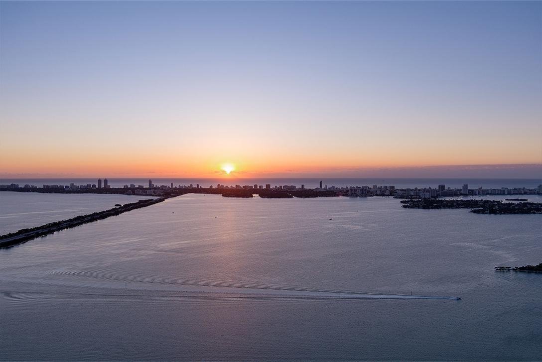 Sunset over a city skyline with water in the foreground and a small boat creating ripples in the water