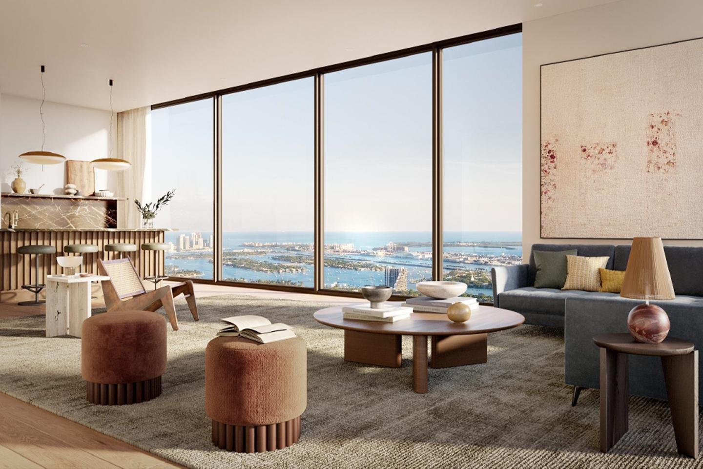 Modern living room with large floor-to-ceiling windows offering city and water views, featuring a gray sofa with colorful pillows, wooden coffee table with decor, pink ottomans, a side table with a lamp, and a dining area with barstools and pendant l