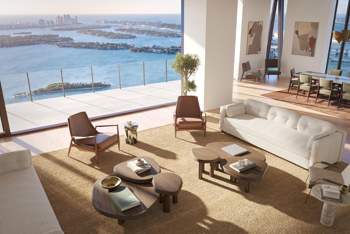 Living room with white couch, two brown armchairs, wooden coffee tables, and a large window overlooking a city skyline and water view.