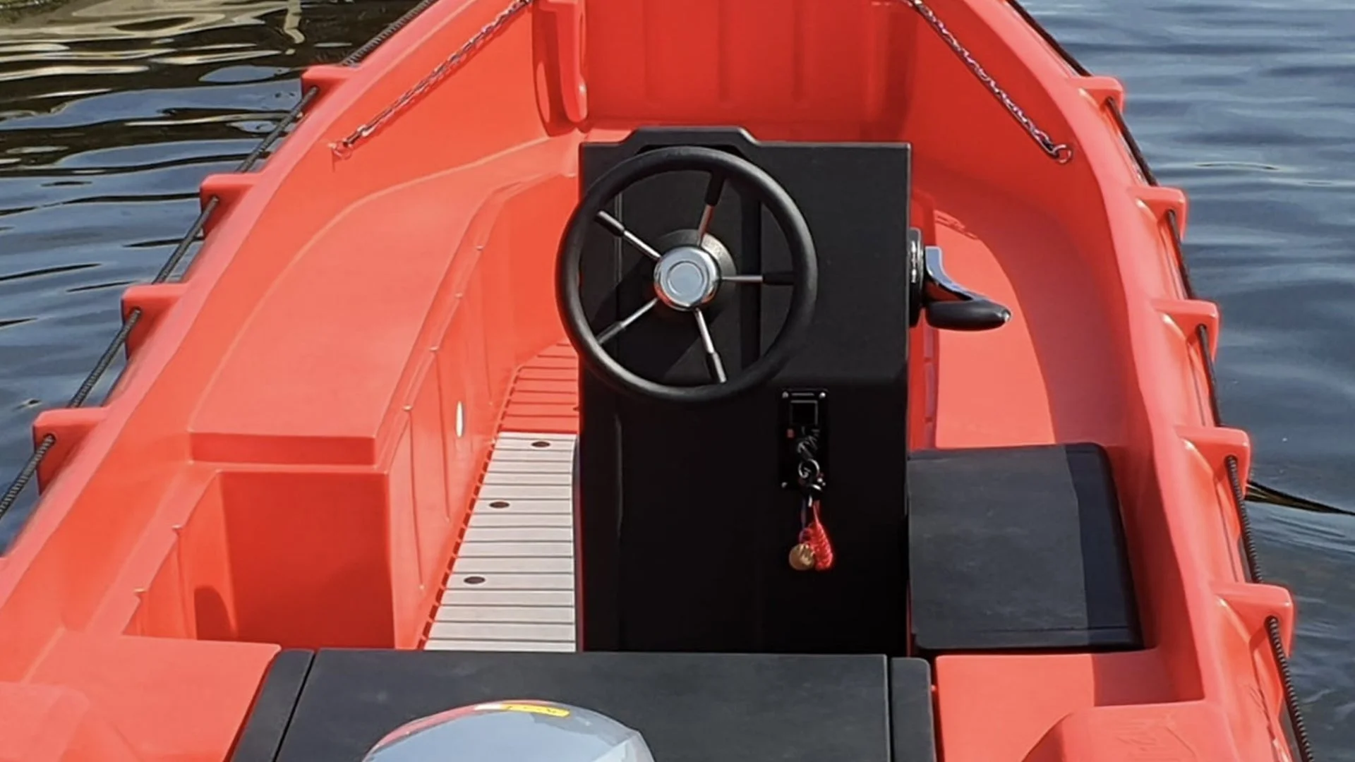 Red inflatable boat on water with black steering wheel and control panel in the center.