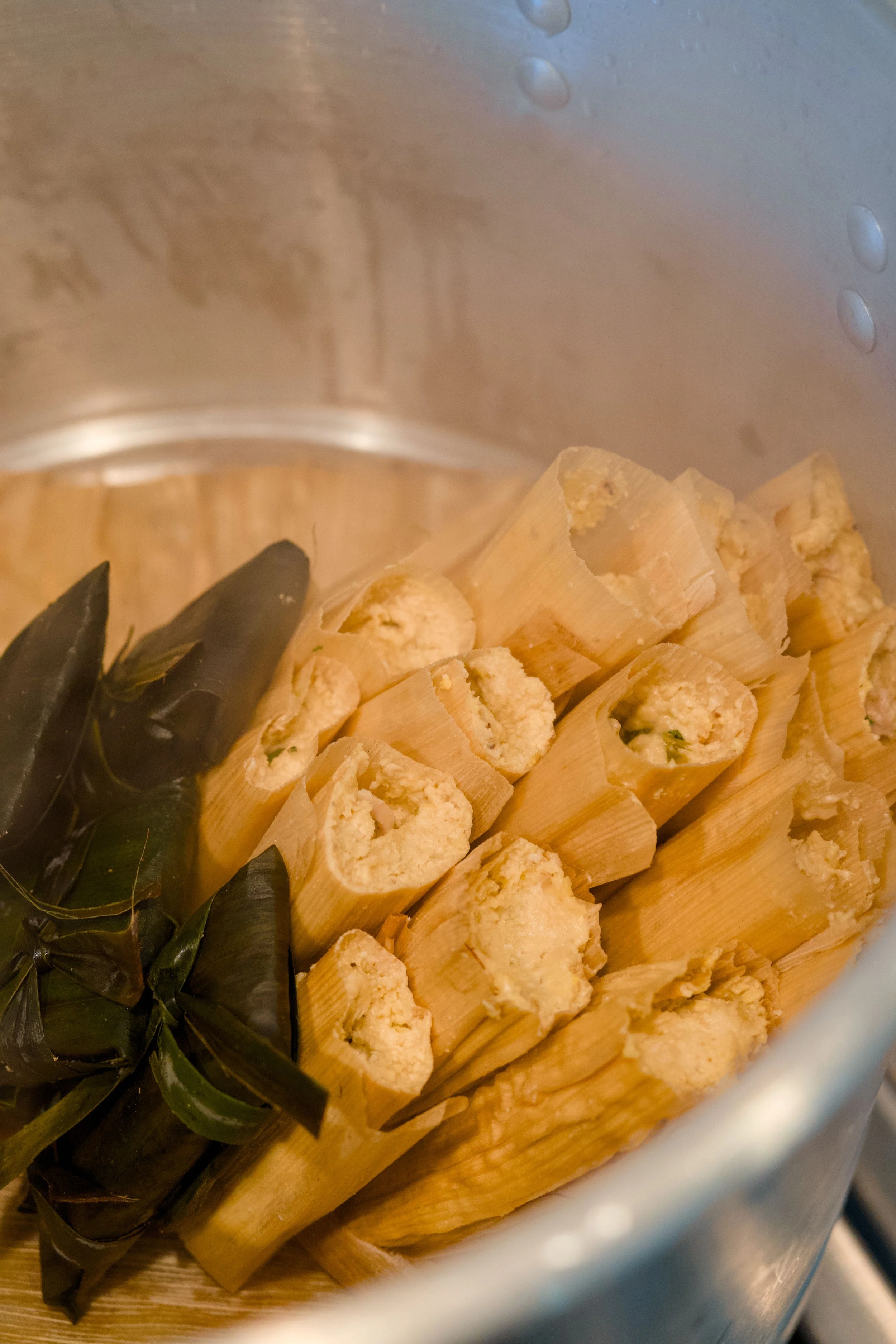 Close-up of tamales wrapped in corn husks and banana leaves in a metal pot.
