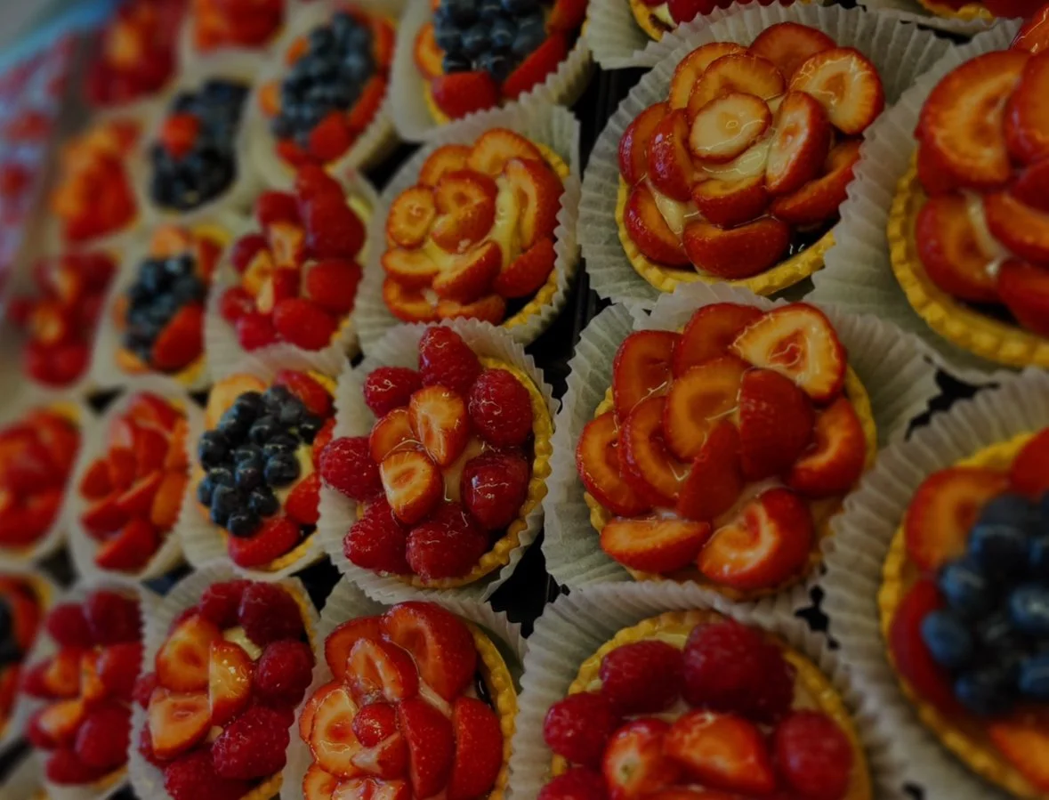 Assorted fruit tarts topped with strawberries, raspberries, blueberries, and sliced strawberries, arranged on a display tray.