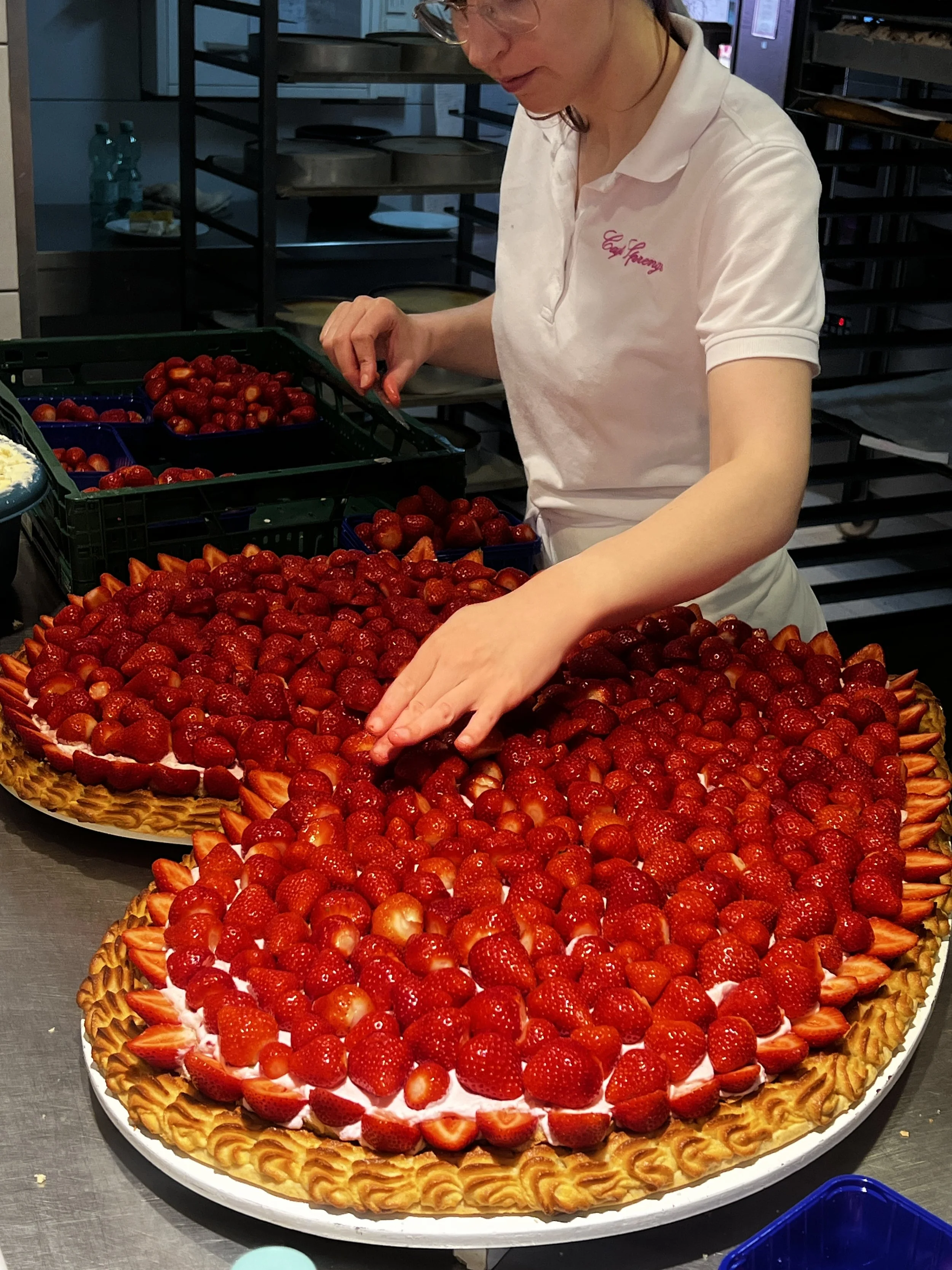 Eine Frau dekoriert in einer Großküche eine große Erdbeertorte mit frischen Erdbeeren.