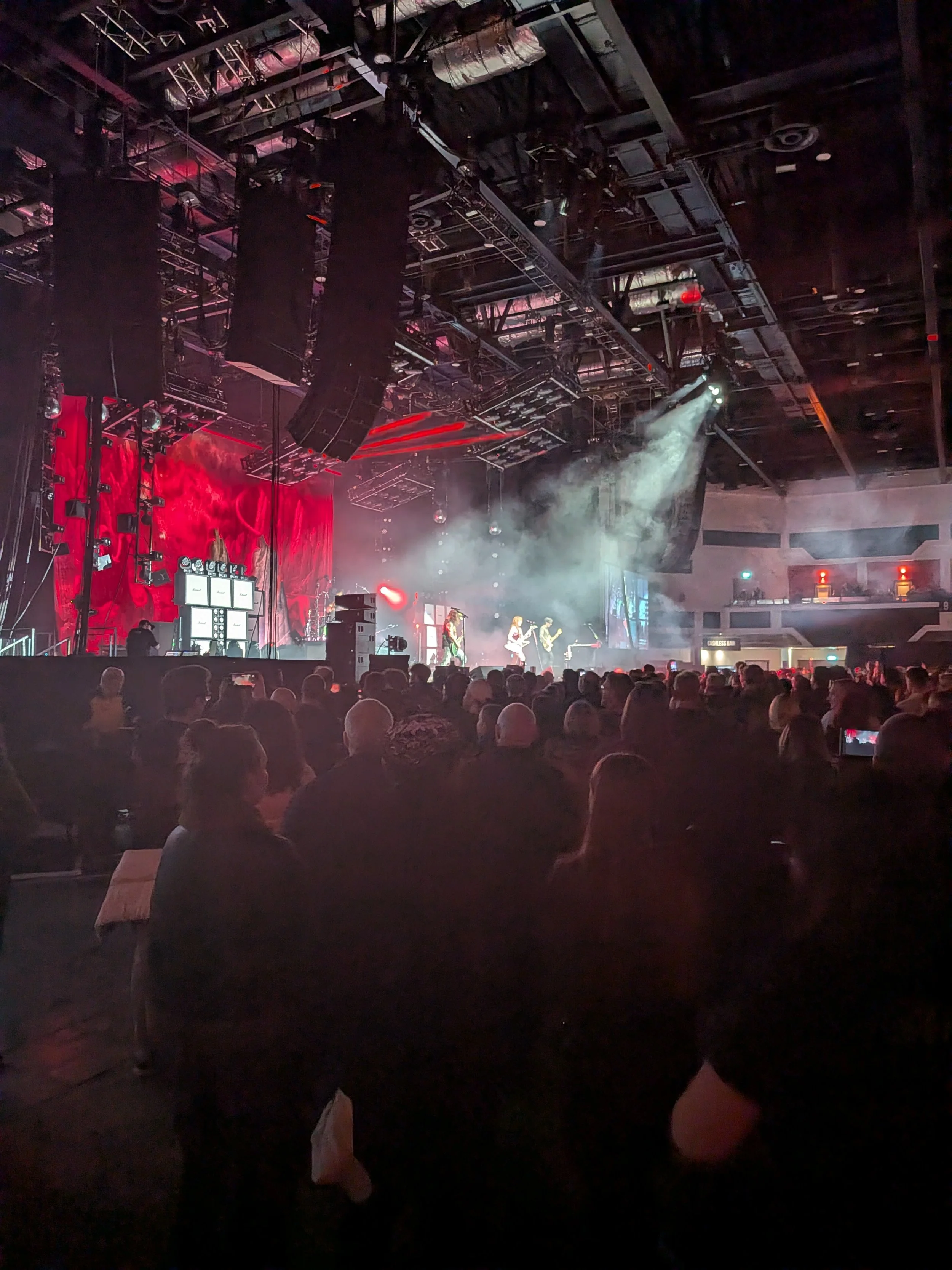 Concert hall with band performing on stage, audience watching, smoke and lighting effects.
