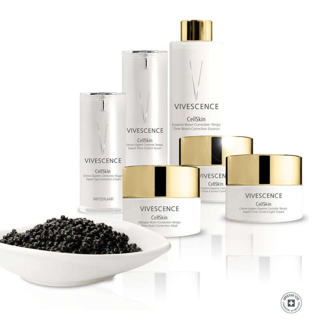 Une gamme de produits de soin pour la peau de la marque VIVESENCE, comprenant différents flacons et pots blancs avec des détails dorés, accompagnés d'une assiette de baies noires.