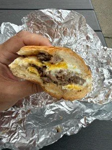 A partially eaten cheeseburger with melted cheese, beef patty, and toppings wrapped in aluminum foil.