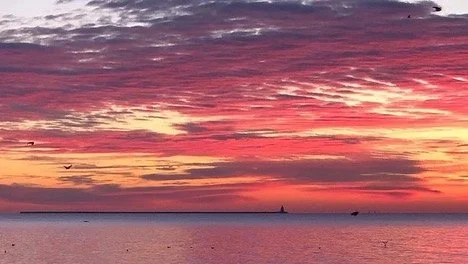 Sunset over the ocean with colorful pink and orange sky and a few small boats in the distance.
