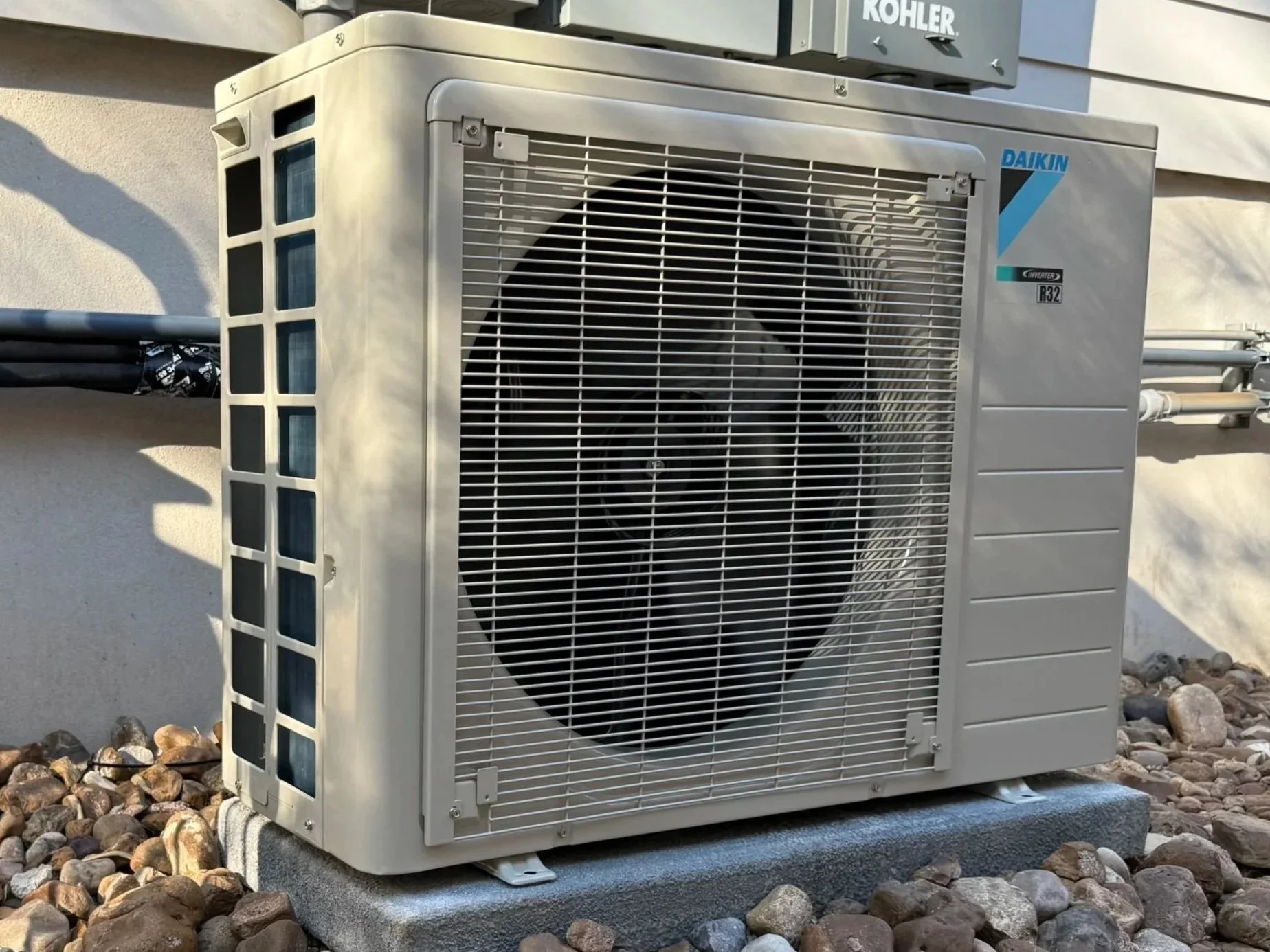 Outdoor air conditioning unit on a concrete pad next to a building wall, surrounded by small rocks.