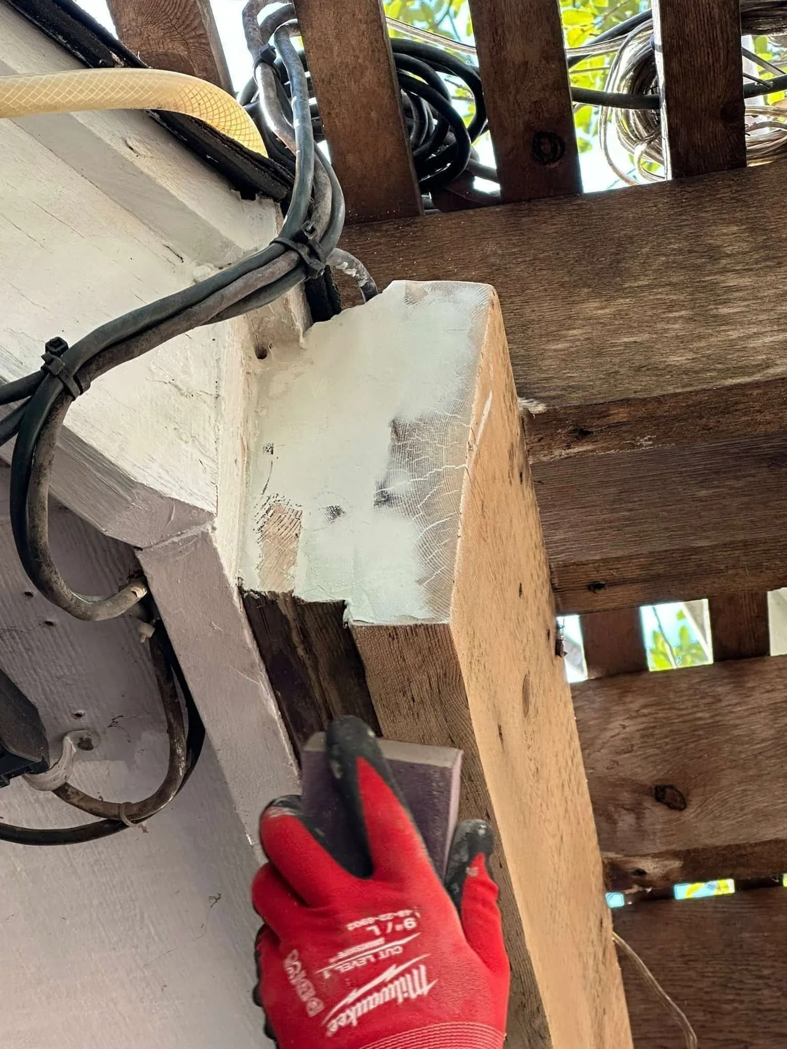 Person wearing a red Milwaukee work glove using a drill on a wooden beam.