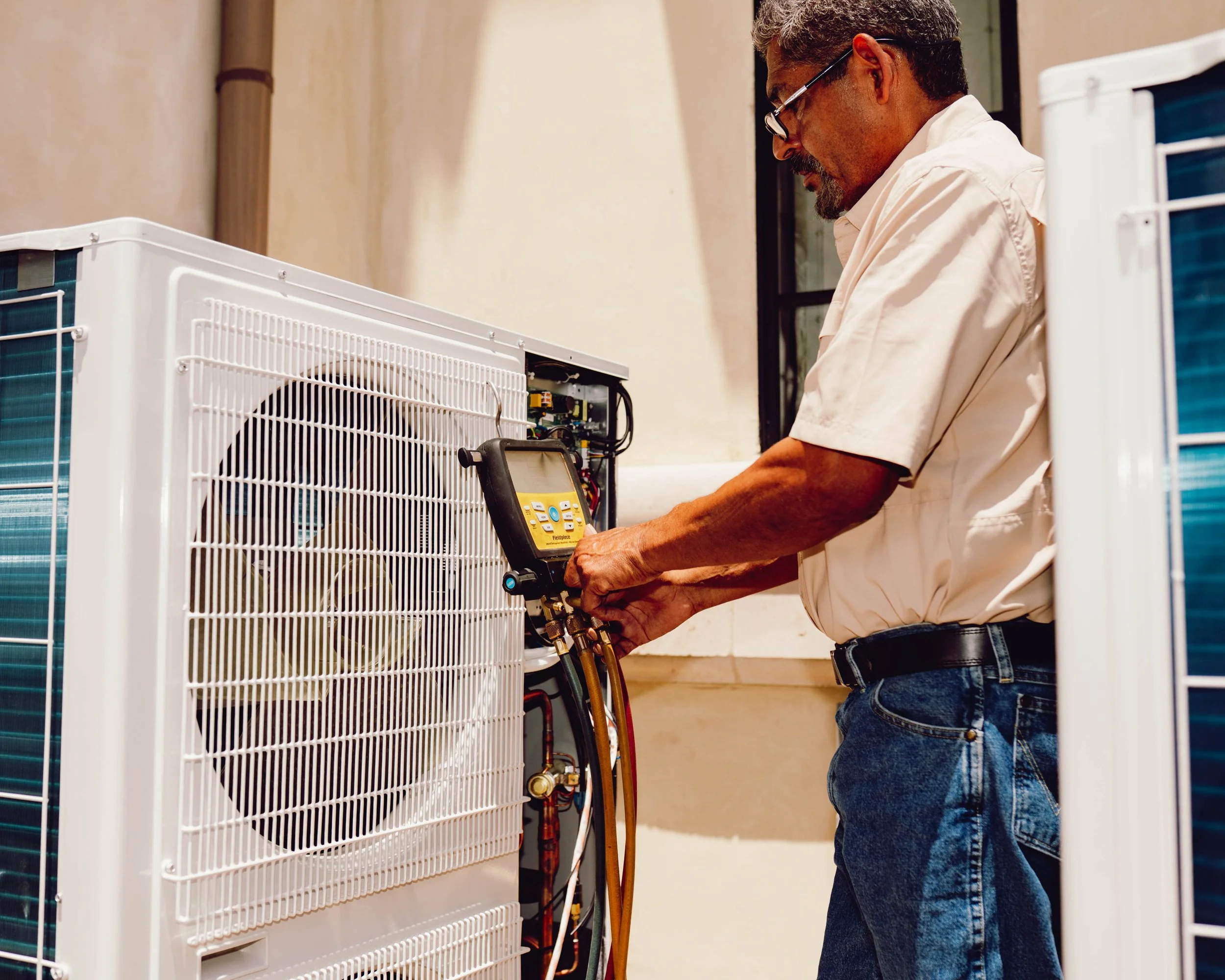 Avanelle Homes Cooling & Heating's lead manager, Fernando, checks the Freon level with a set of digital gauges while performing maintenance on a high efficiency side discharge AC system with the new refrigerant installed in a lake house Lake LBJ, TX.