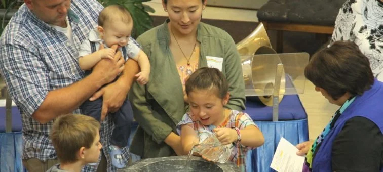 Group of people, including children and adults, gathered around a water fountain in an indoor setting.